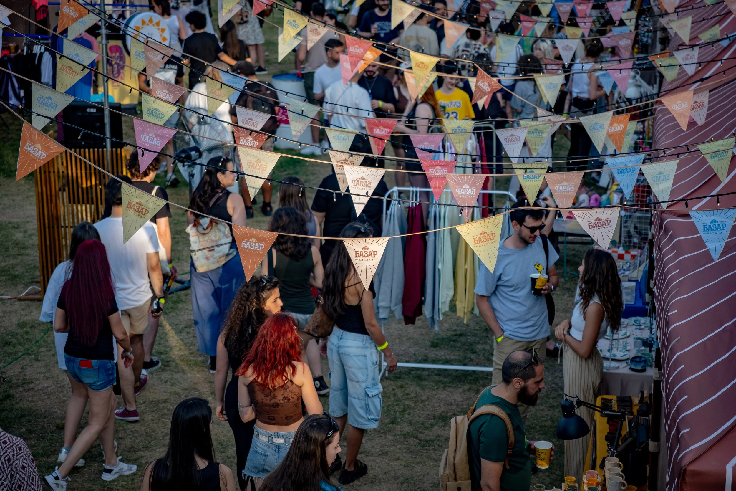 Crowd of people attending outdoor festival with colorful triangular banners hanging above.