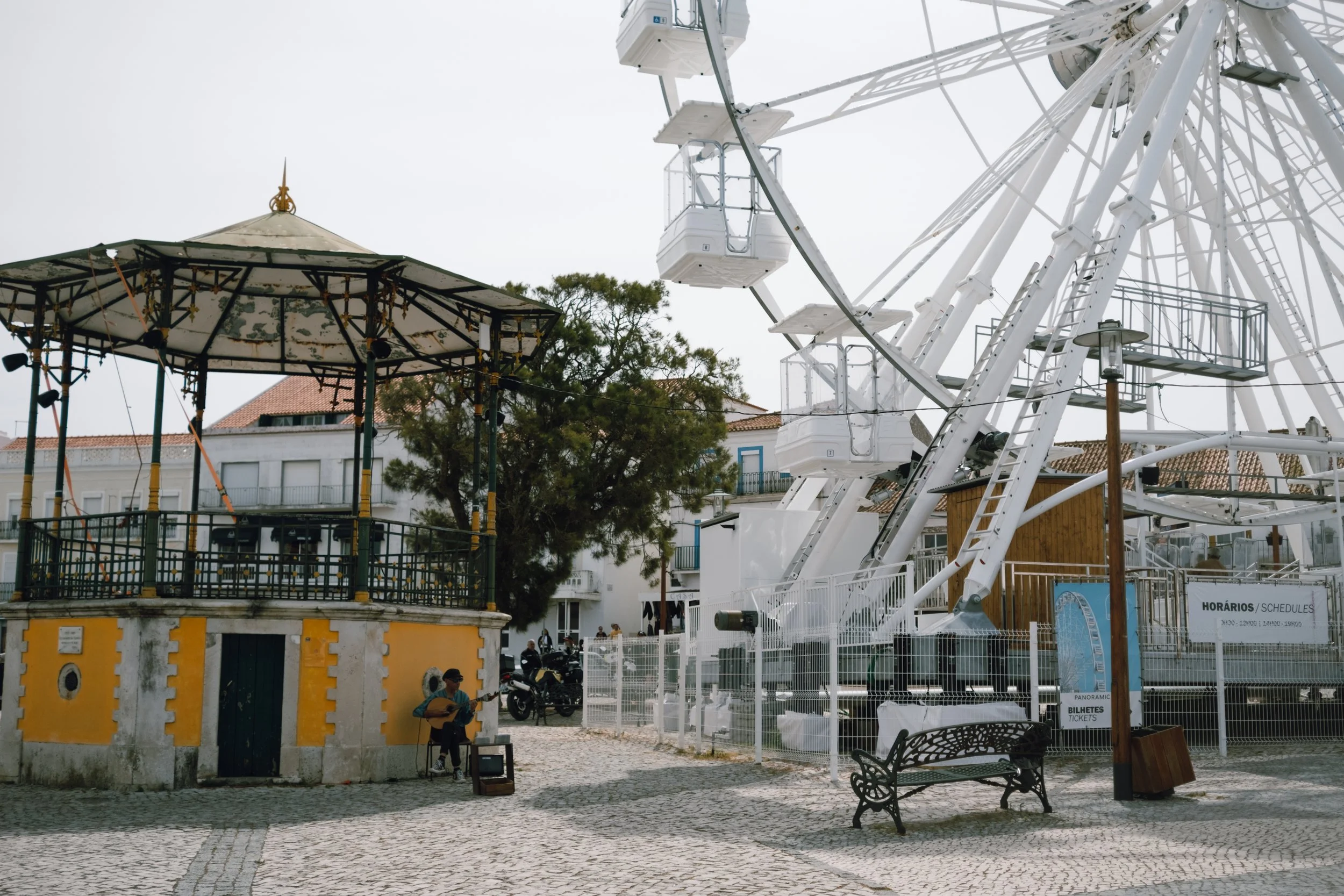 A small yellow and white carousel next to a large white Ferris wheel in an outdoor amusement park.