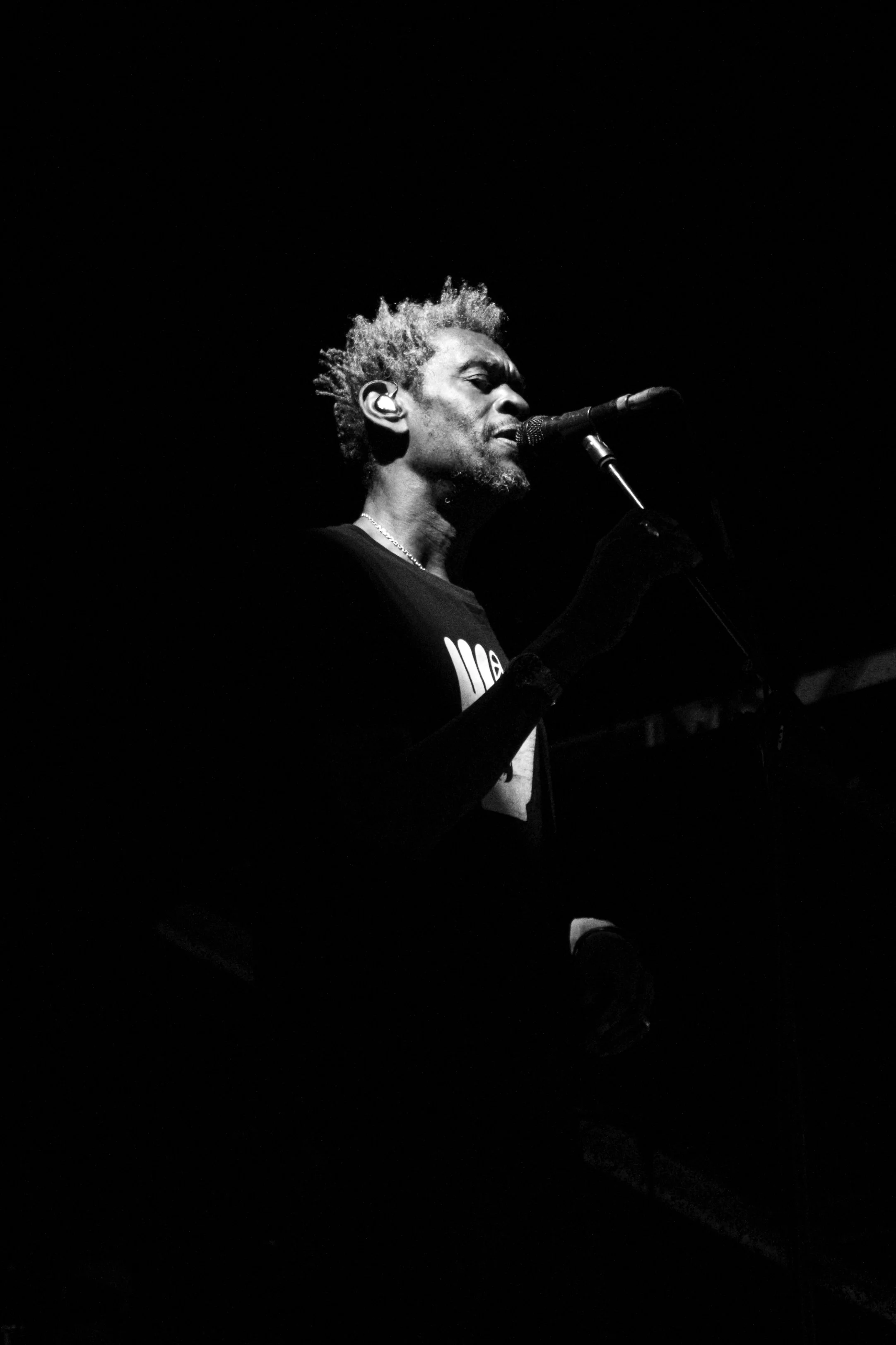 Concert Photographer captured Massive Attack playing at Sofia Live Festival. A black and white photo of a male singer performing on stage, singing into a microphone, with dark background and focused lighting on his face and upper body.