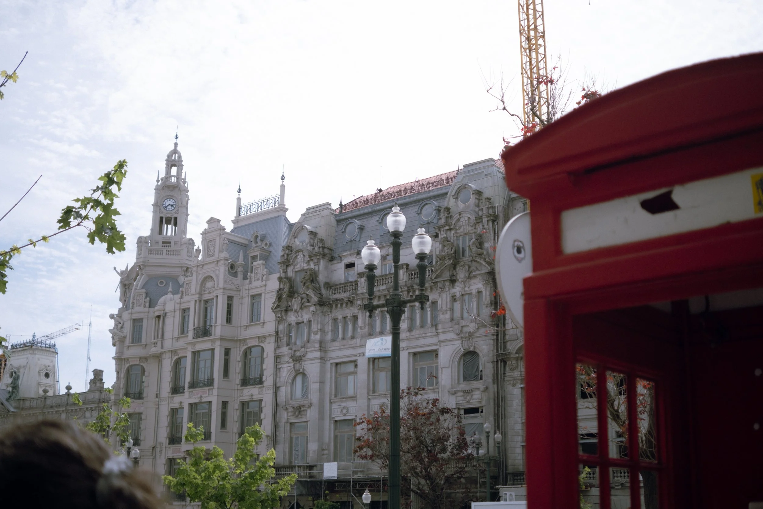A historic ornate white building with decorative architecture, a clock tower, and multiple statues on the facade, partially obscured by a red phone booth and streetlamp in the foreground.