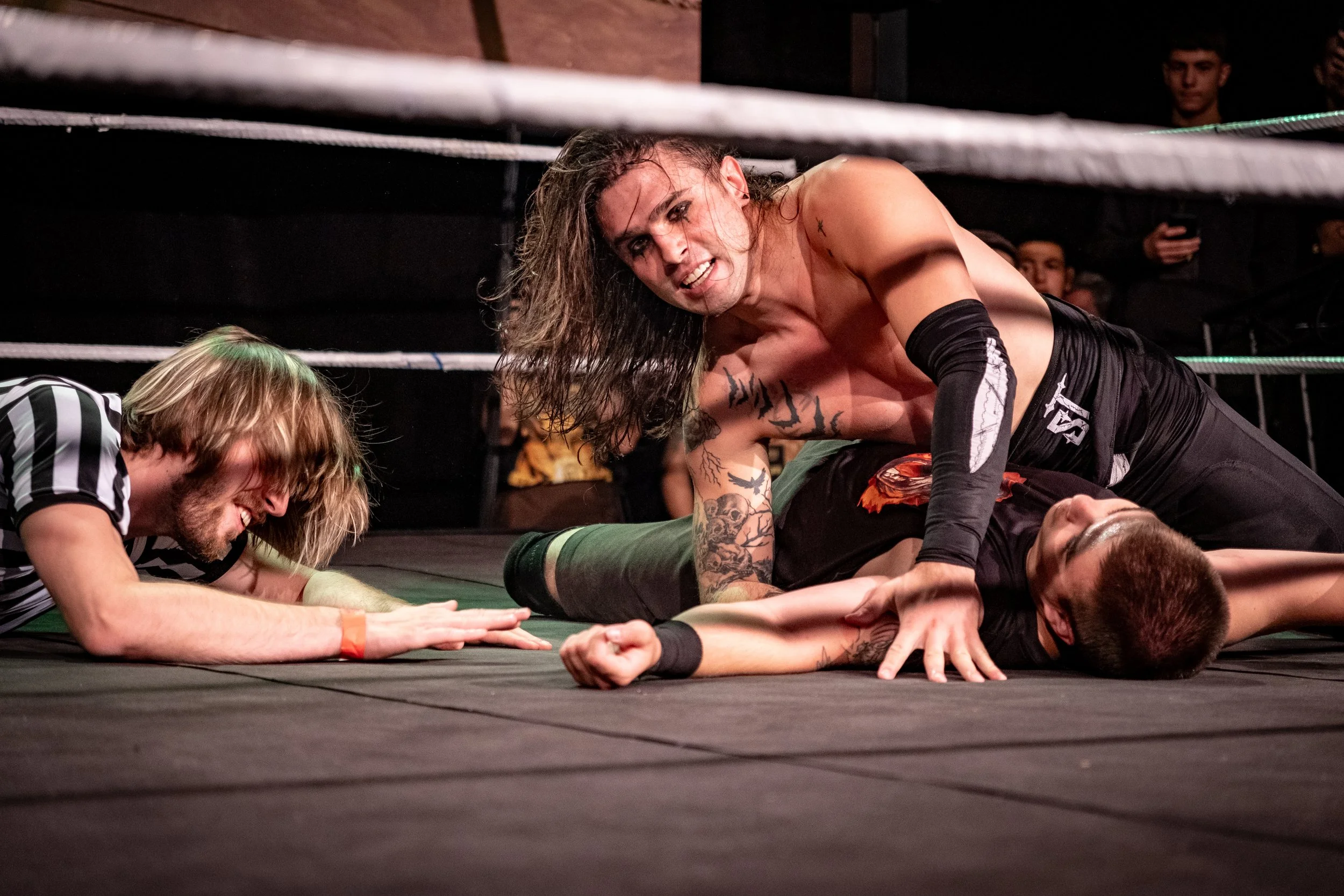 Wrestling match with two competitors on the mat and a referee nearby.
