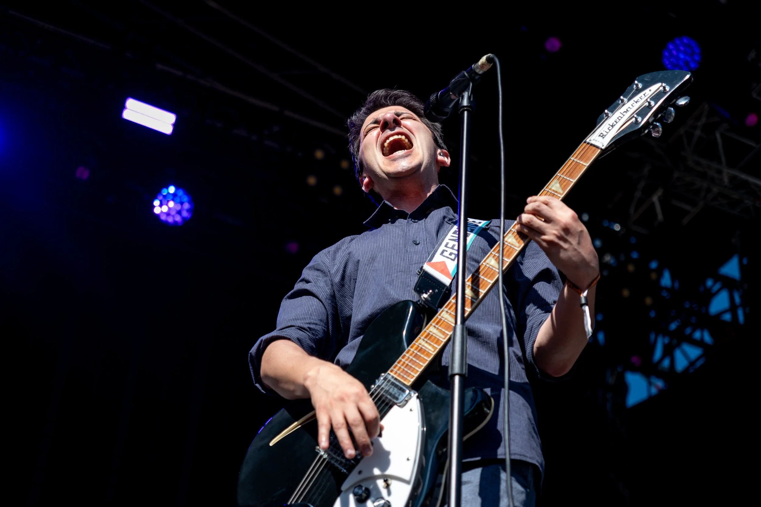 Musician passionately singing and playing electric guitar on stage at a concert with dark background and purple and blue stage lights.