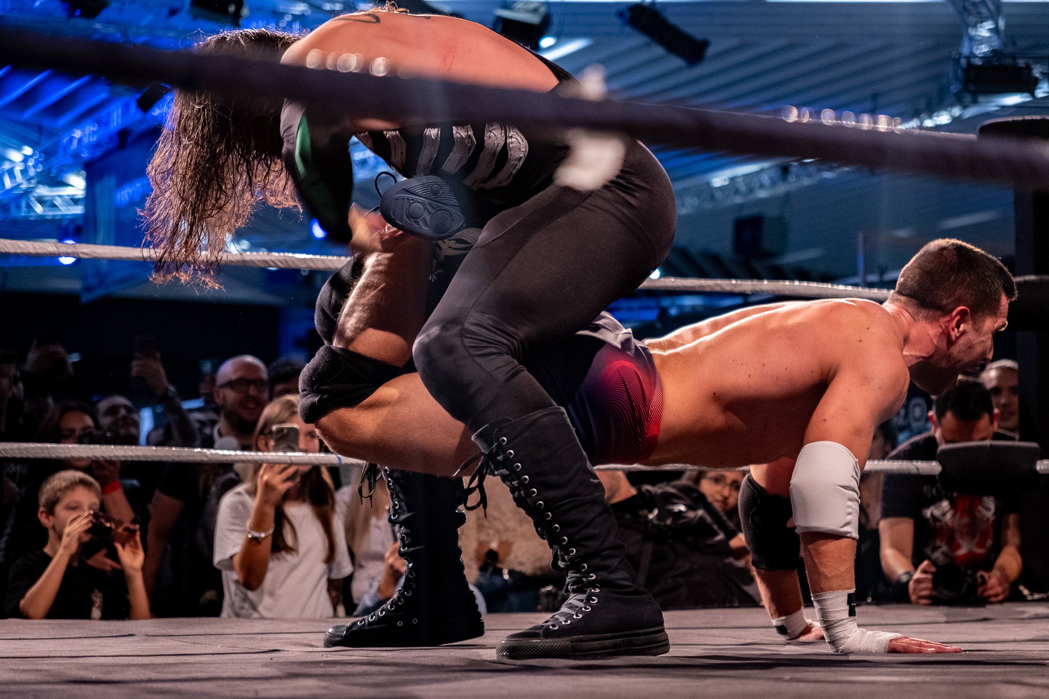 A wrestling match with a woman on top of a man in a ring surrounded by an audience.