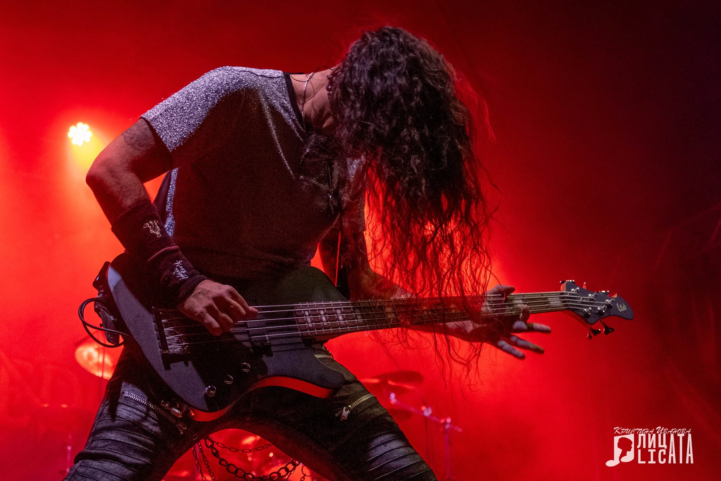 Musician playing electric bass guitar on stage with red lighting.