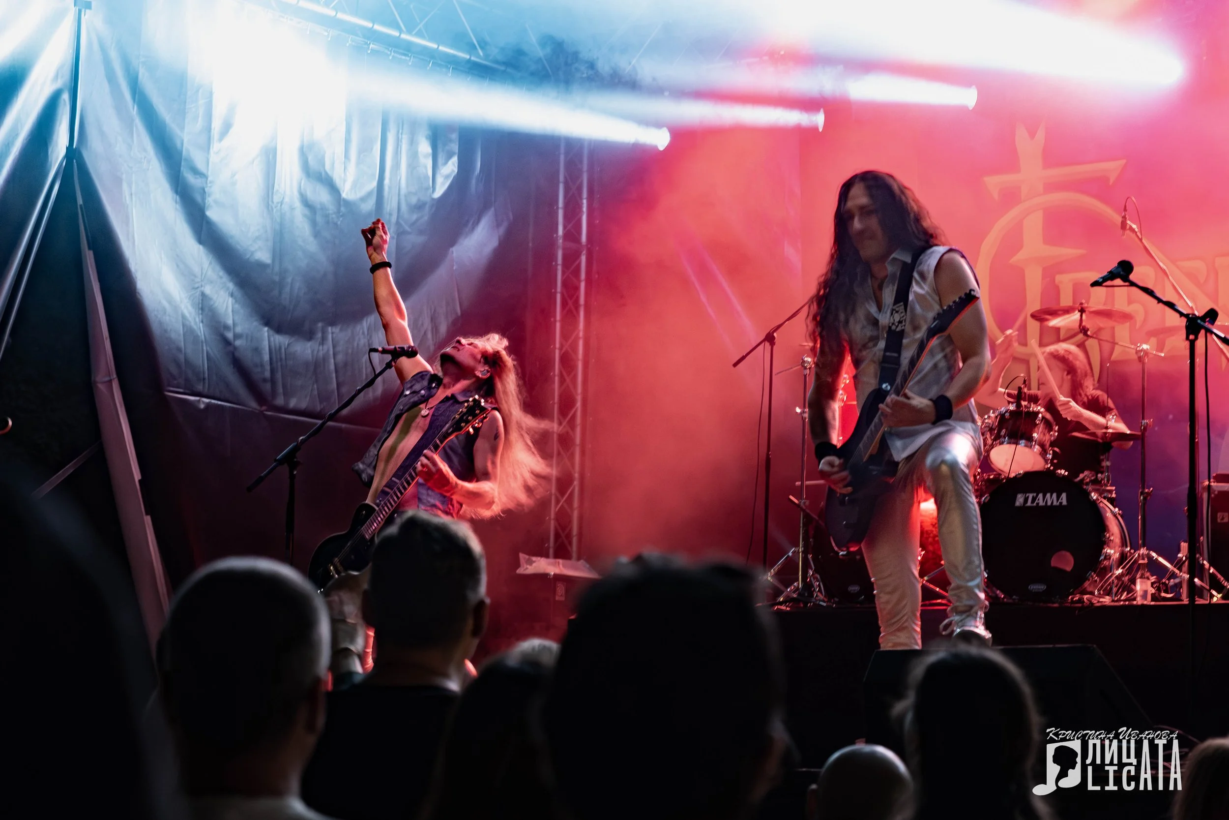 A rock band performs on stage in front of an audience, with bright stage lights and smoke effects.