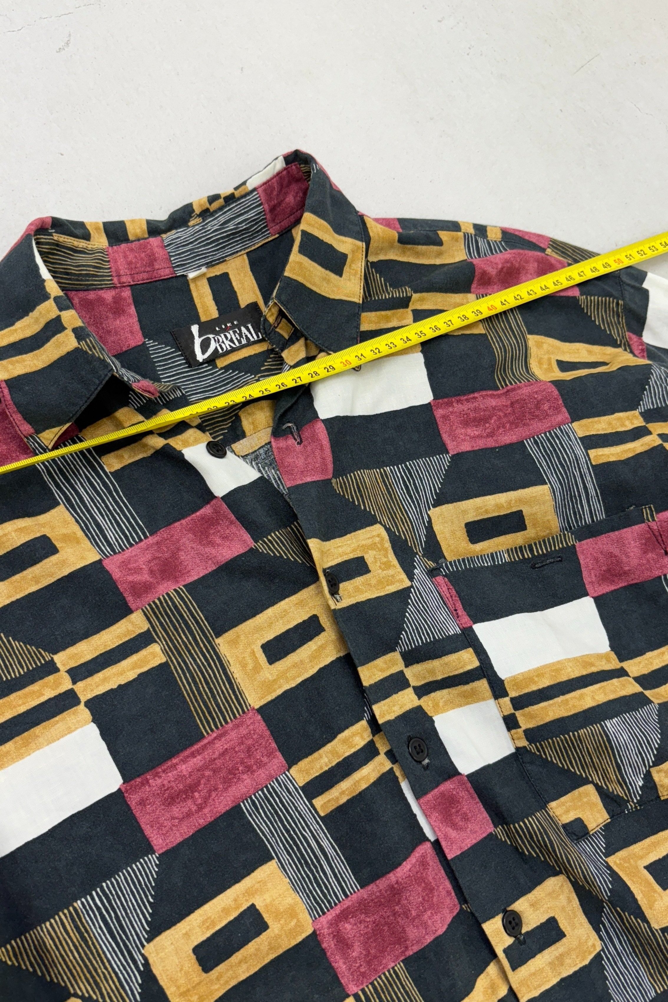 A flat lay of a vintage Italian menswear shirt showcasing its unique print and high-quality fabric showing the measurements..