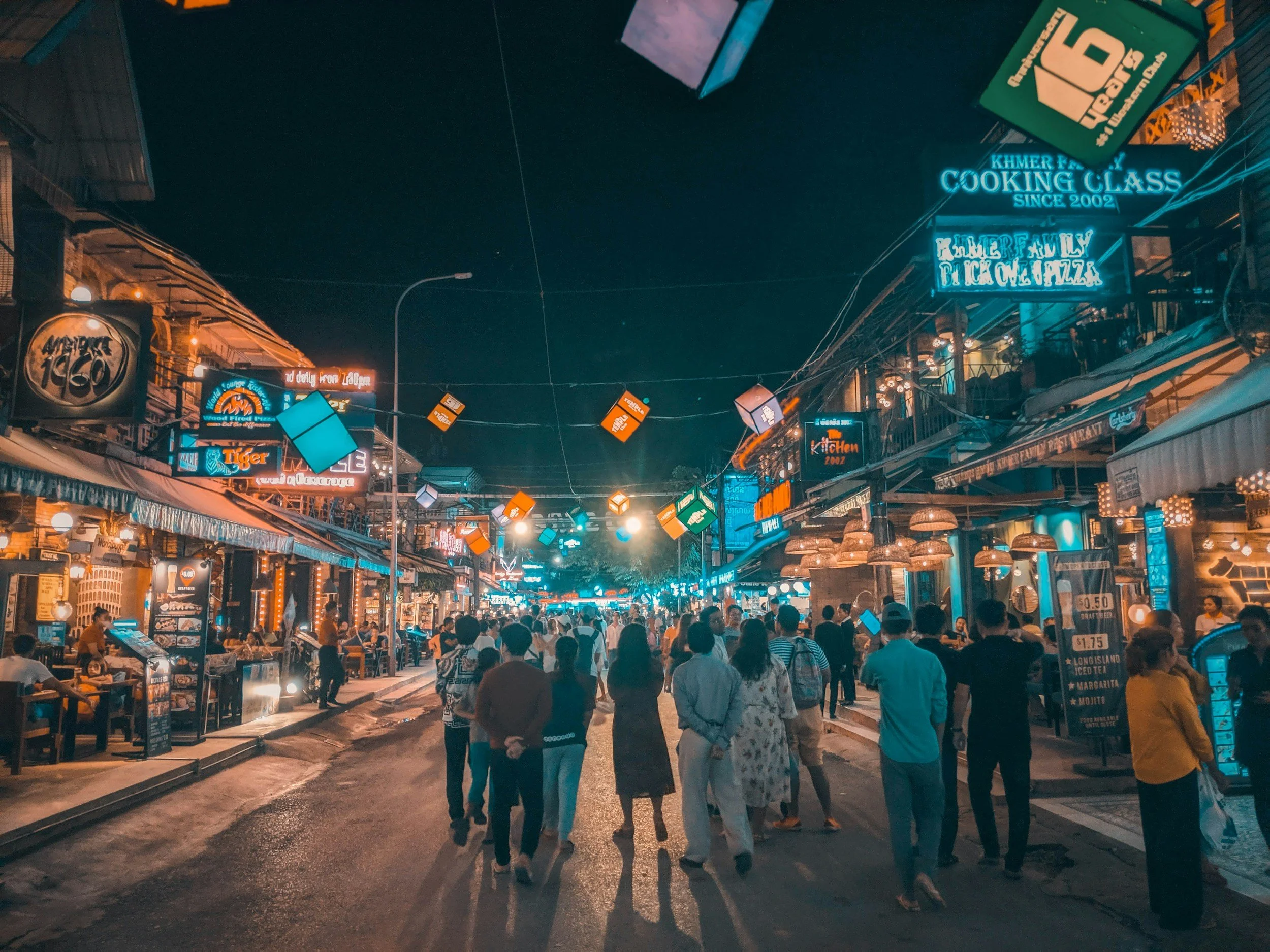 Nighttime view of Pub Street. A busy street lined with restaurants and shops, illuminated by neon signs.