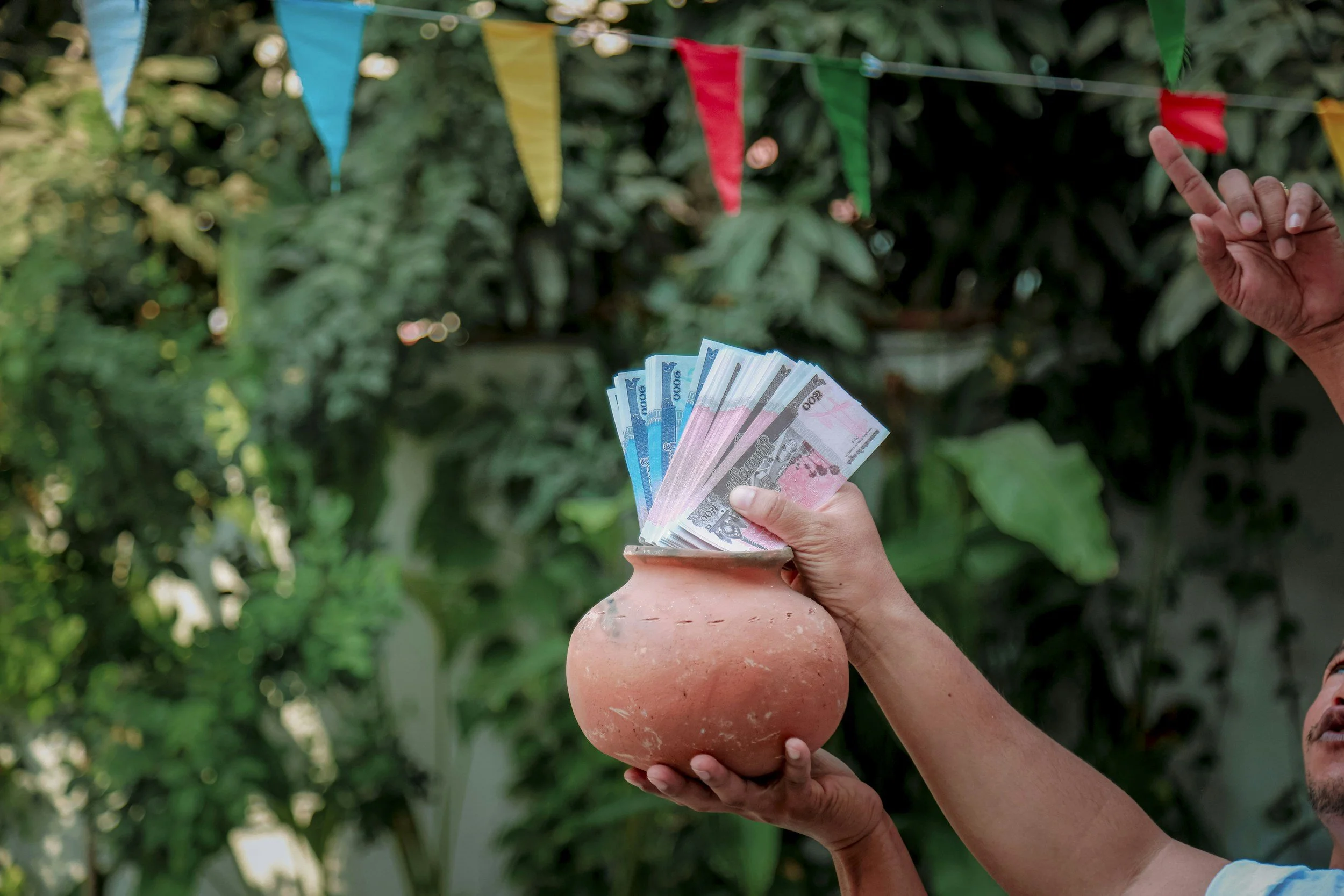 A person holding a clay pot filled with blue and pink paper currency notes, traditional Khmer tradition