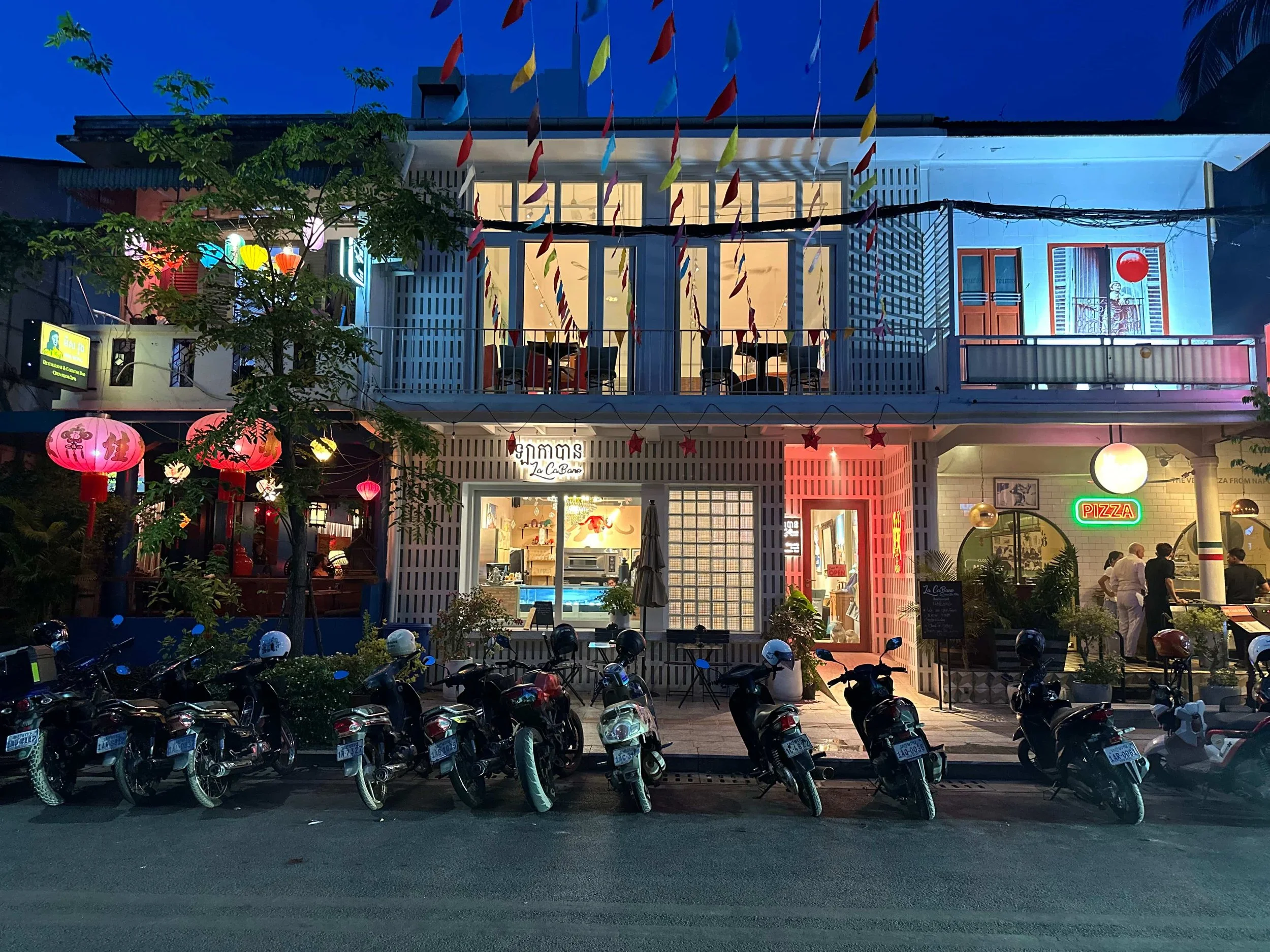 Siem Reap shophouse restaurants on Street 26 in Wat Bo Village at dusk with lanterns and motorbikes.