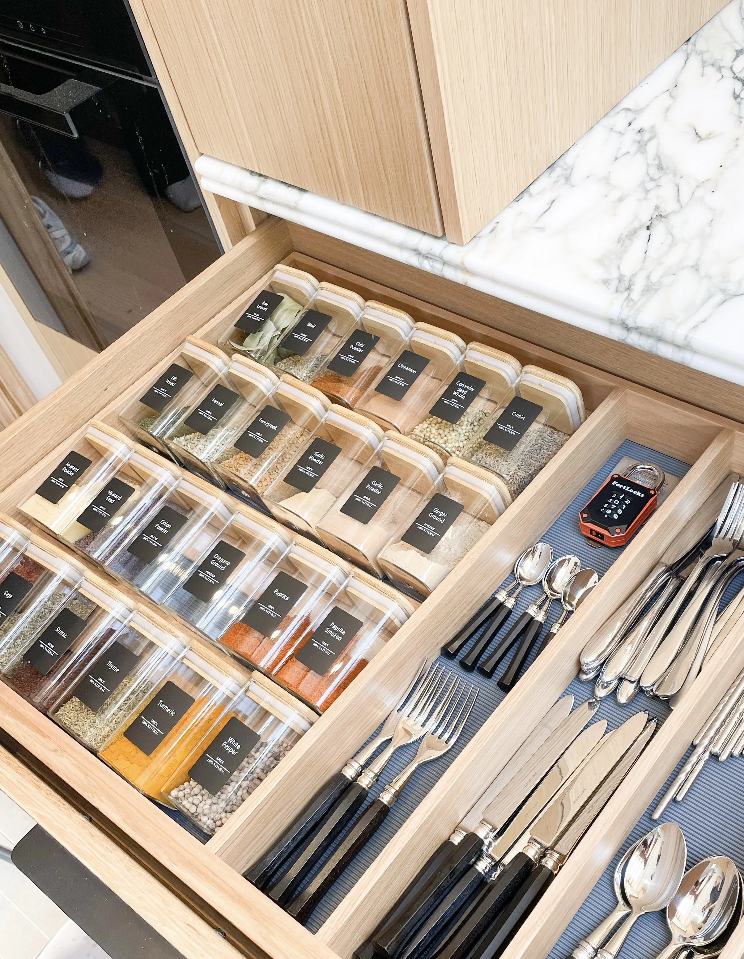 Drawer filled with neatly arranged, labelled spice jars for easy access and organised storage.