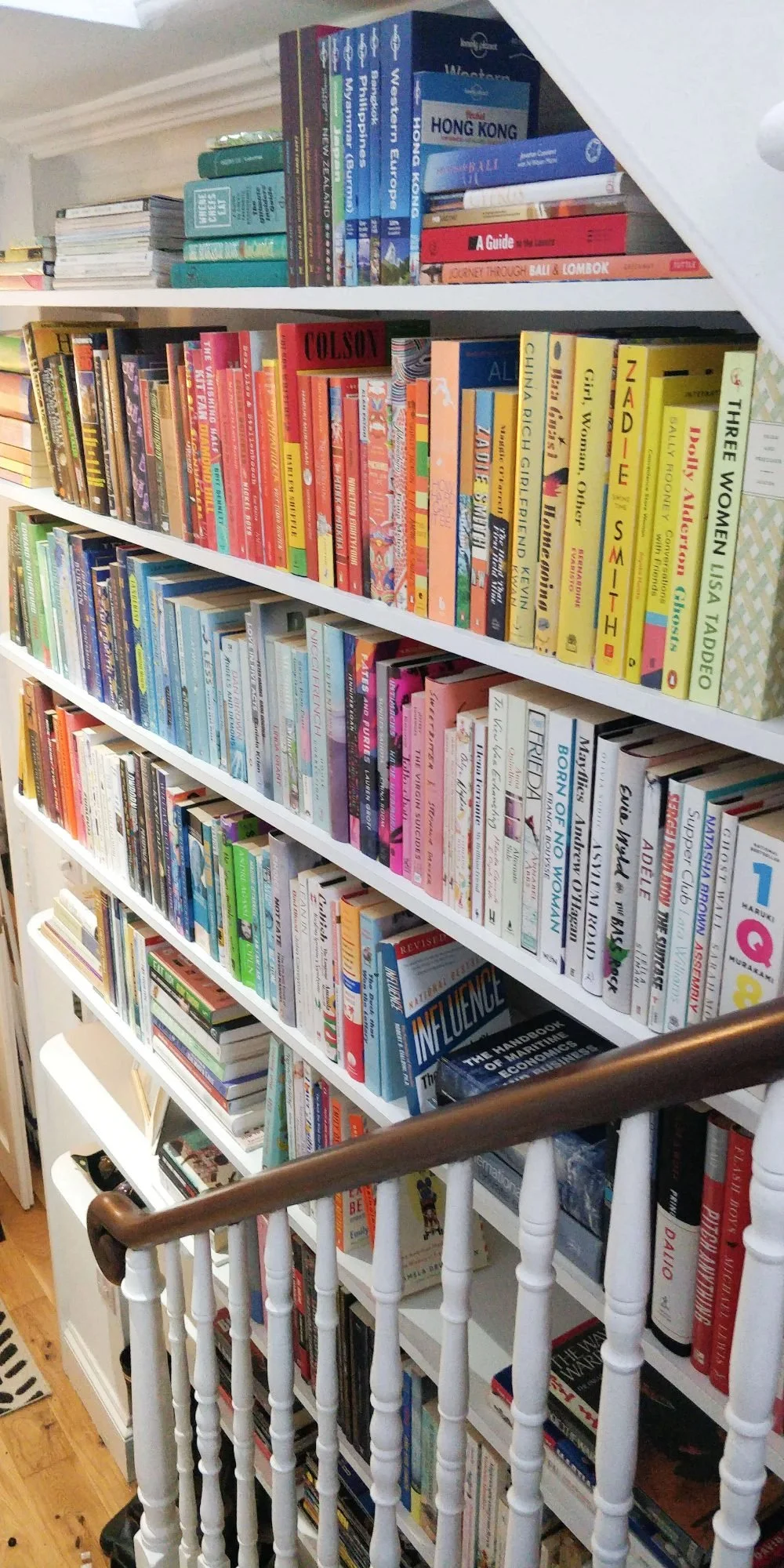 A colour-organised bookshelf covers the wall next to the stairs