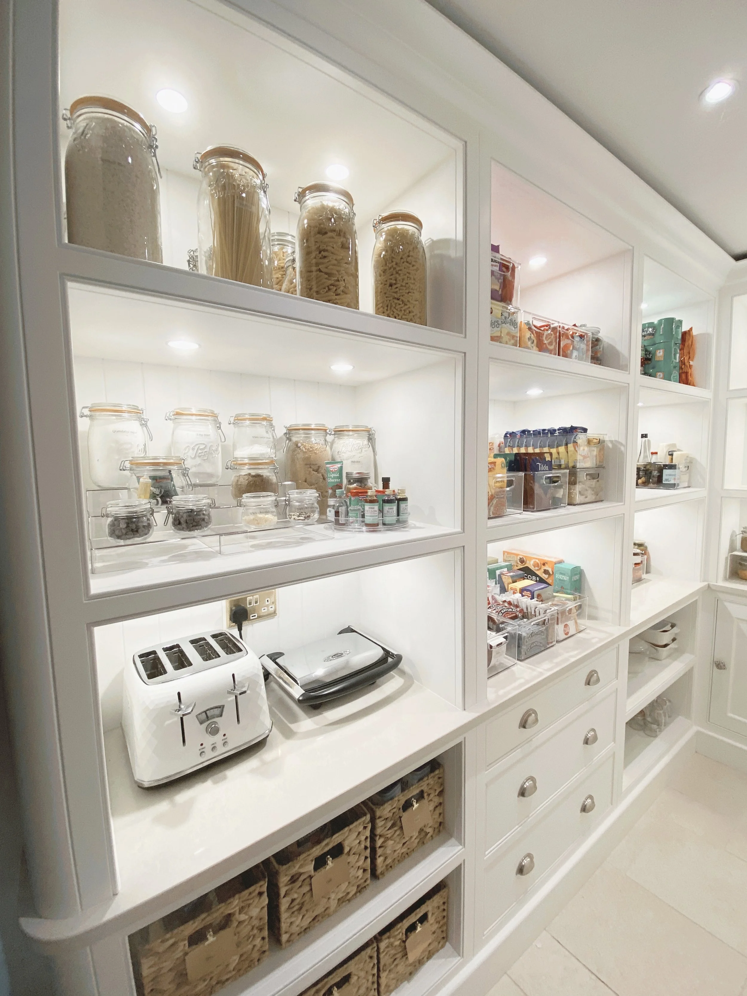 Walk-in pantry with decanted food in labelled containers and neatly organised food bins arranged on open shelving.