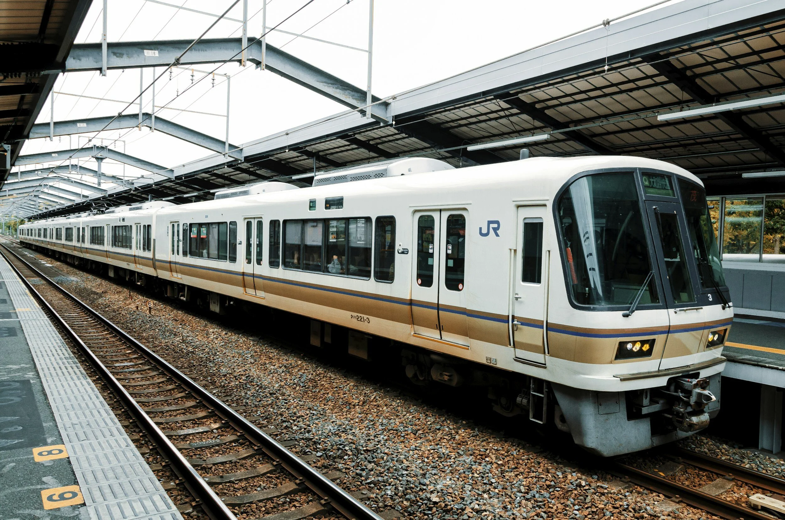 A white train with blue and orange stripes at a train station platform, with tracks and a covered station roof overhead.