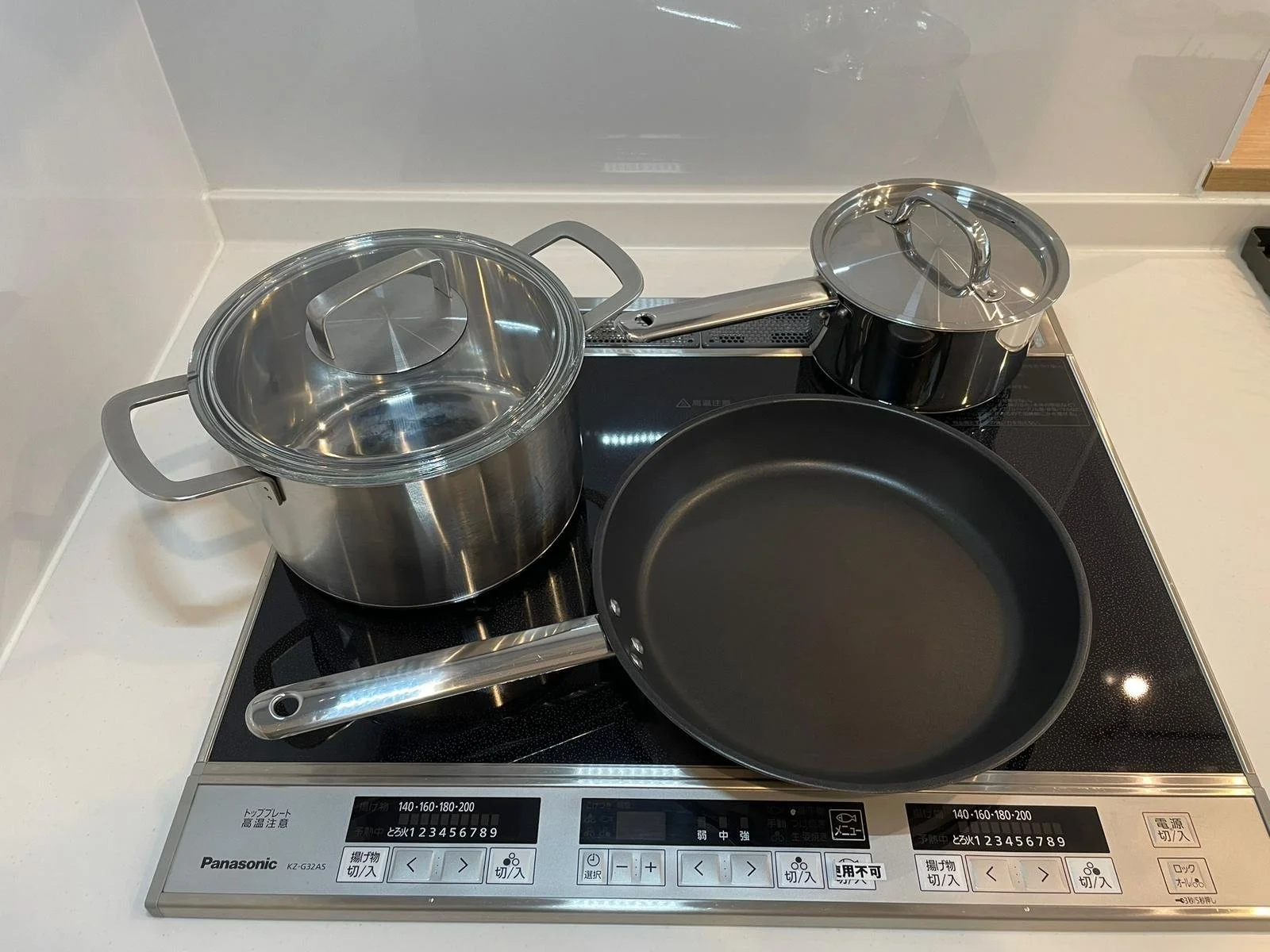 A modern electric stove with three pots and a frying pan. The stove has a digital control panel and is situated on a white countertop.