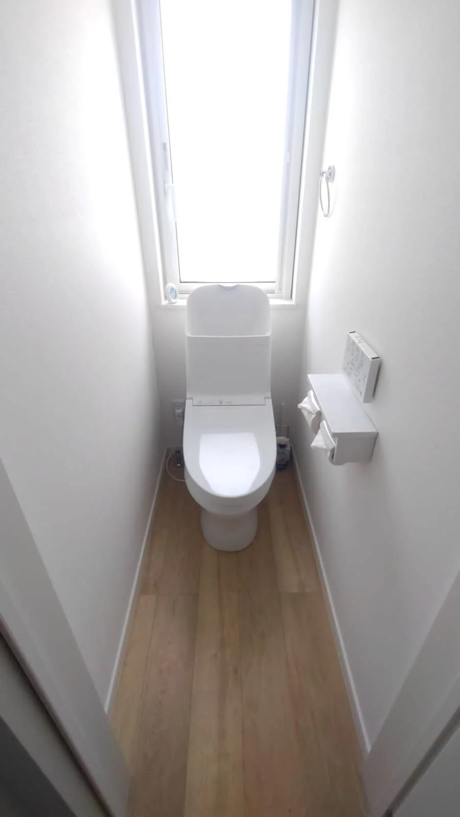 A small, white bathroom with a modern toilet facing a frosted window.