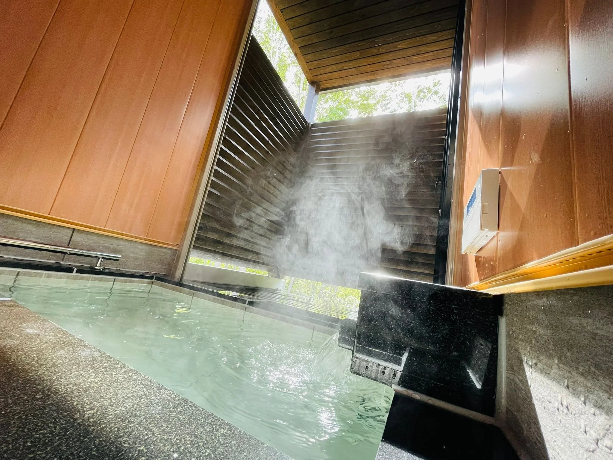 Indoor hot tub with bubbling water, steam rising, wood-paneled walls, and an outdoor balcony with wood railing.