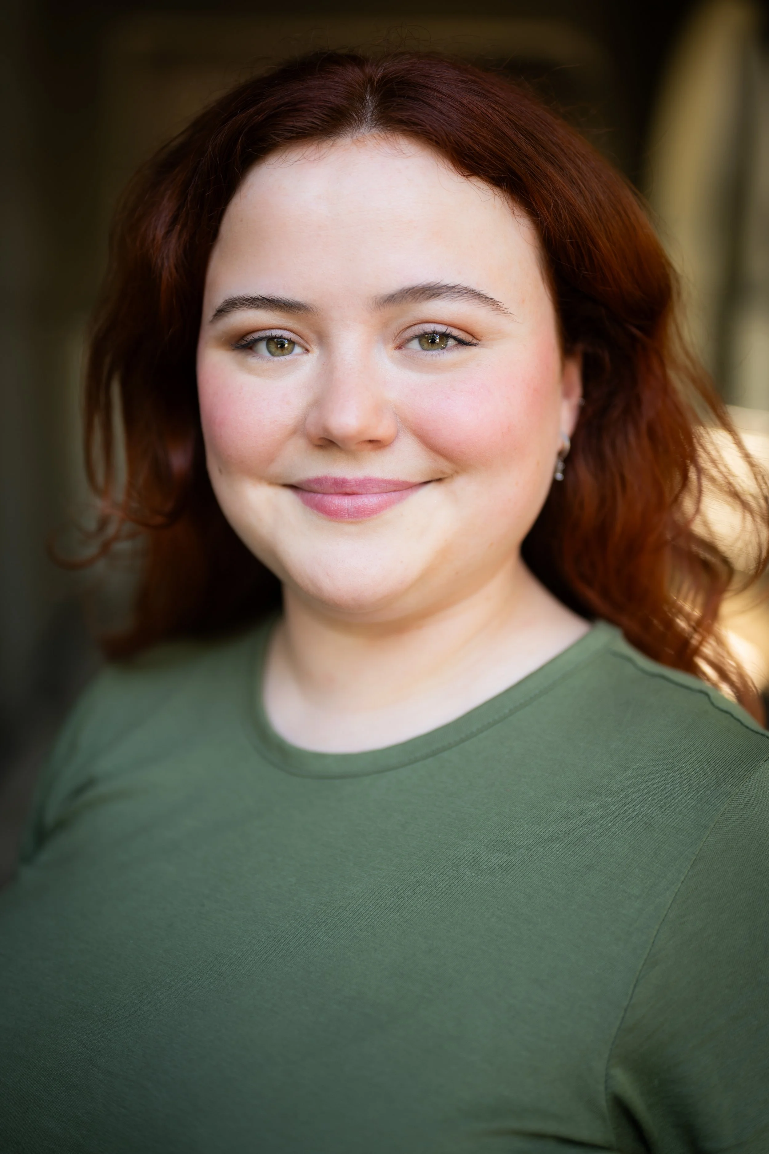 Portrait of a woman with red hair, wearing a green shirt, smiling outdoors.