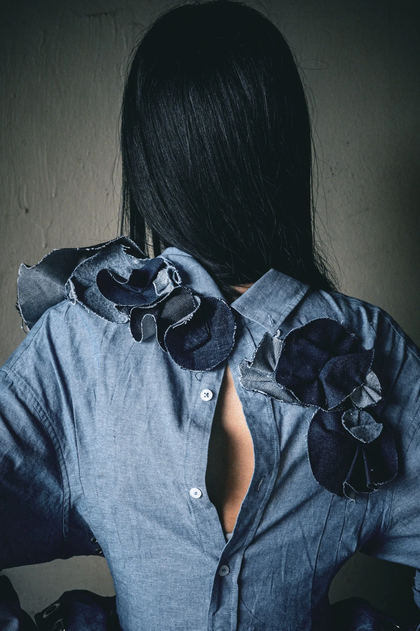 A woman with straight black hair wearing a denim shirt with flower embellishments on the shoulders.