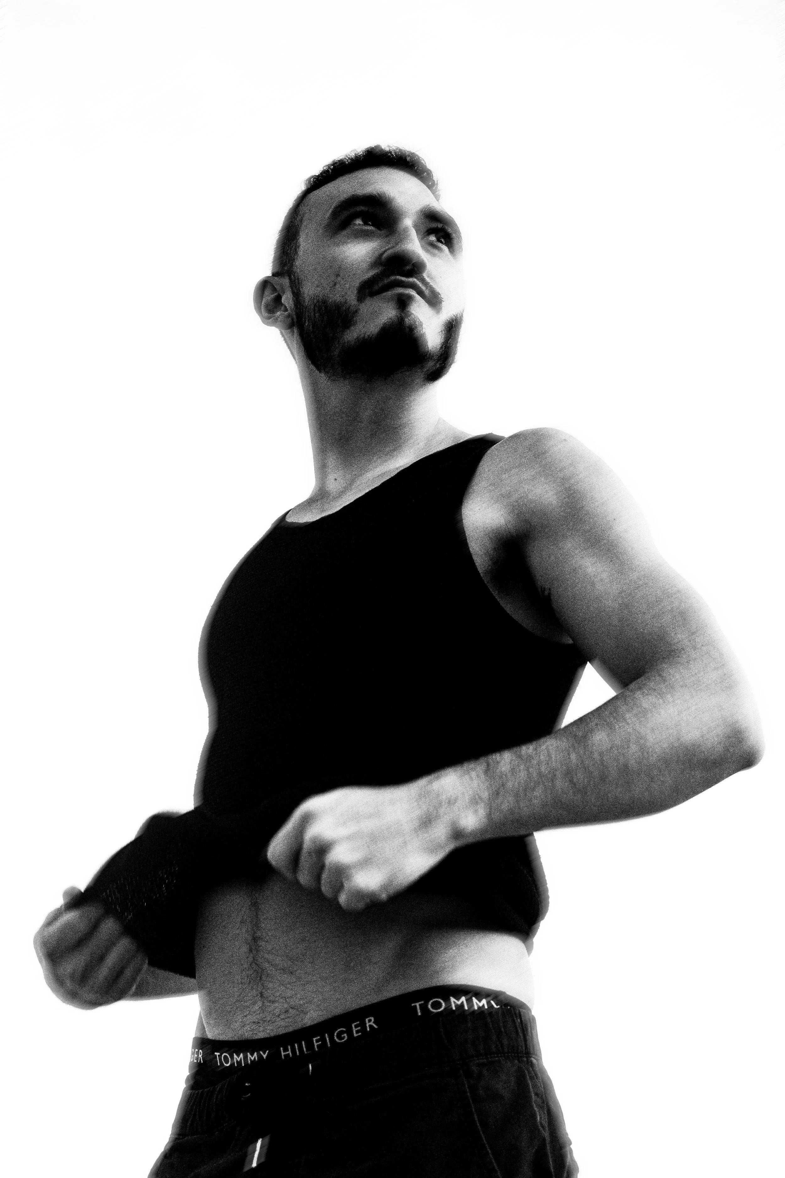 A black and white photo of a man lifting his black T-shirt to show his abdomen.