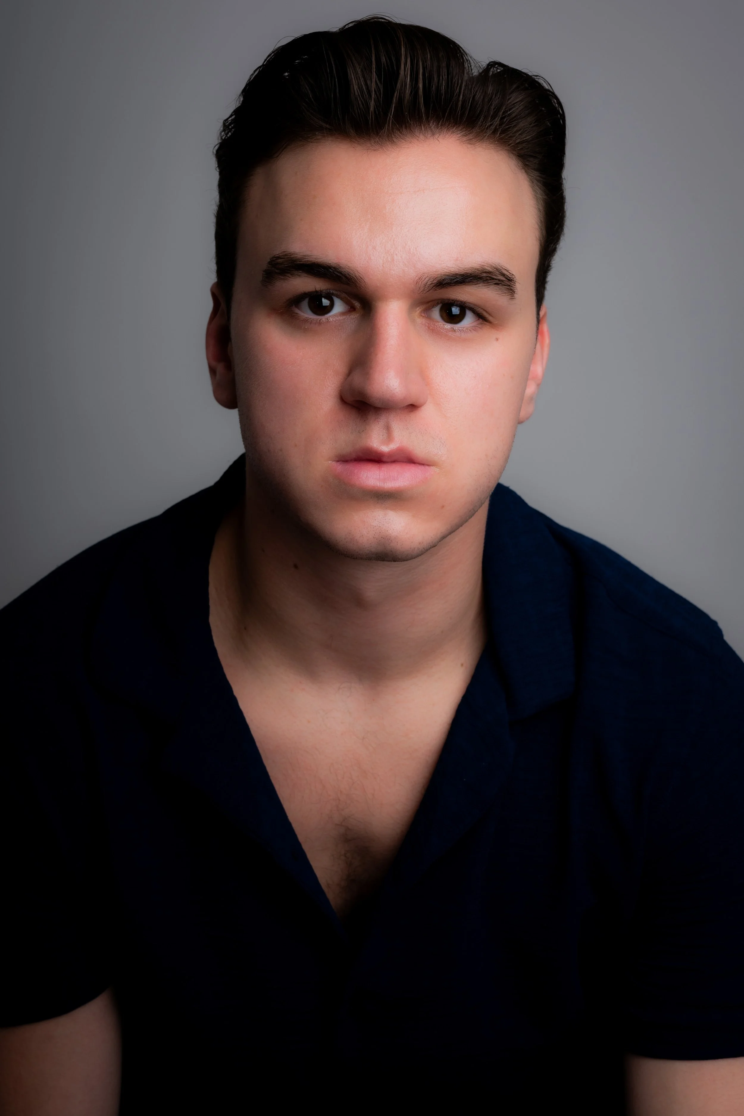 Portrait of a young man with dark hair, wearing a black shirt, against a gray background.