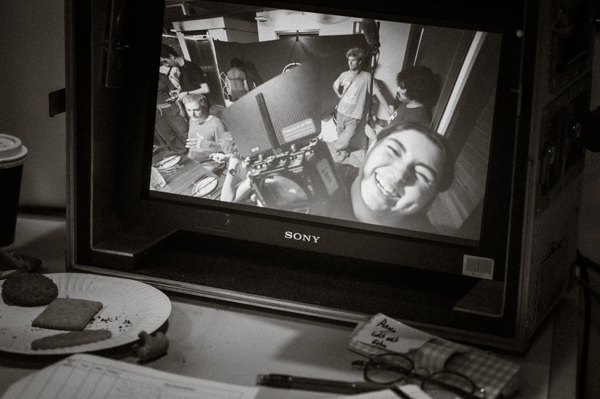 Black and white photo of a Sony monitor displaying the upside-down image of a smiling woman, with several people in the background.