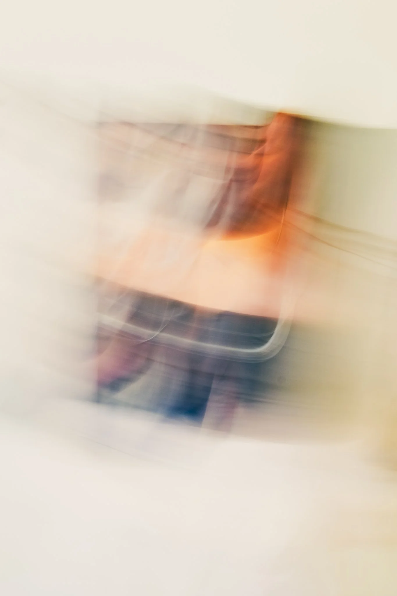 A blurry image of a person taking a selfie with a smartphone. The person has dark hair and is wearing a light-colored shirt and dark pants. The image is intentionally out of focus with motion blur.