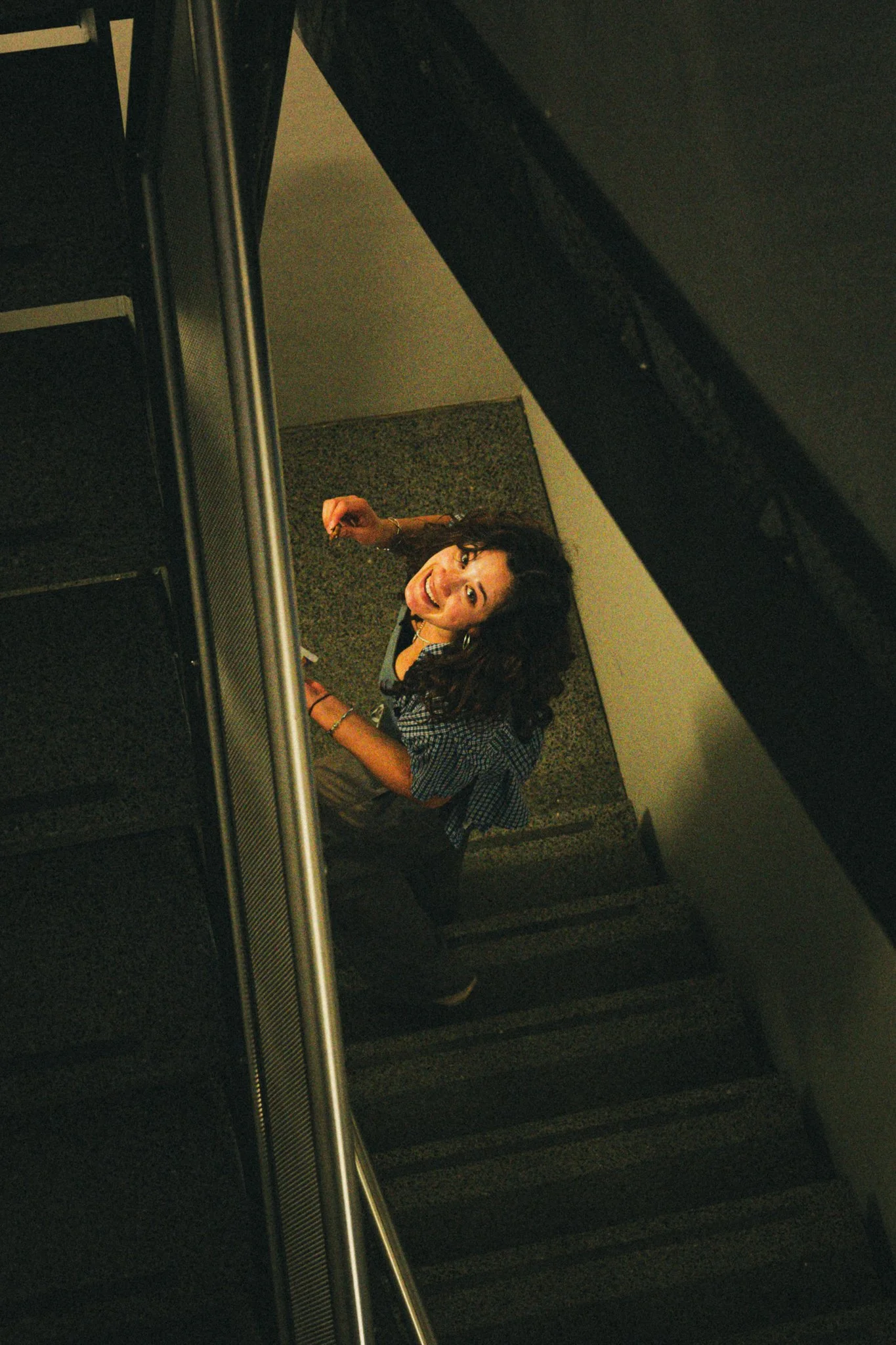 A smiling woman with curly hair looking up at the camera while riding an escalator.