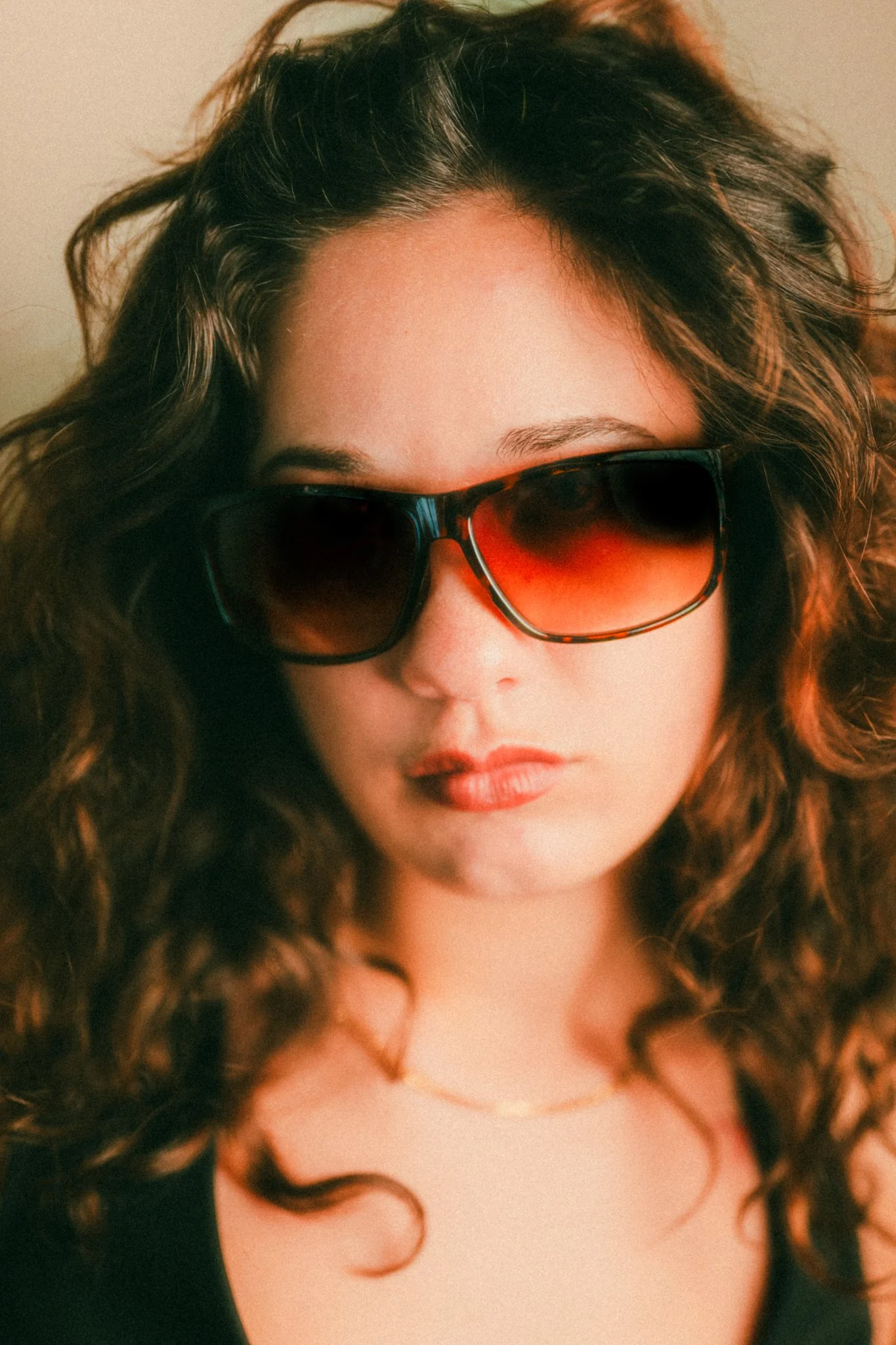 A woman with curly hair wearing large, orange-tinted sunglasses and a black top.