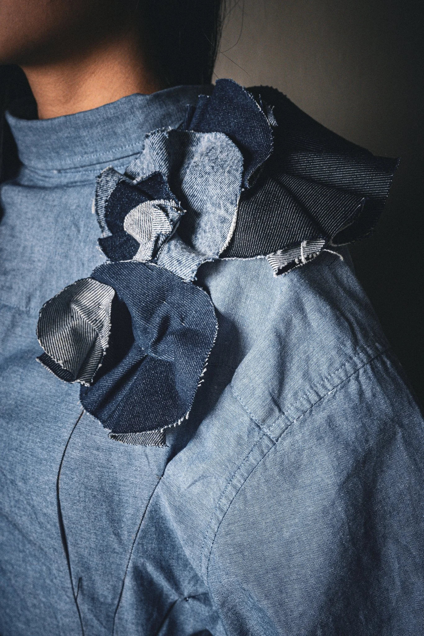 Close-up of a person wearing a denim shirt with fabric flower embellishments on the shoulder.