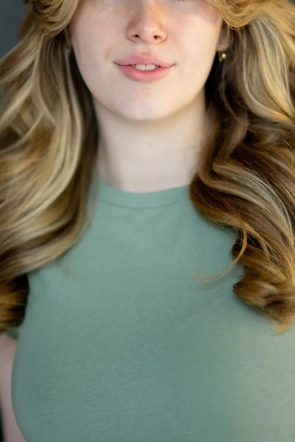 Close-up of a smiling woman with long, wavy blonde hair wearing a light green top.
