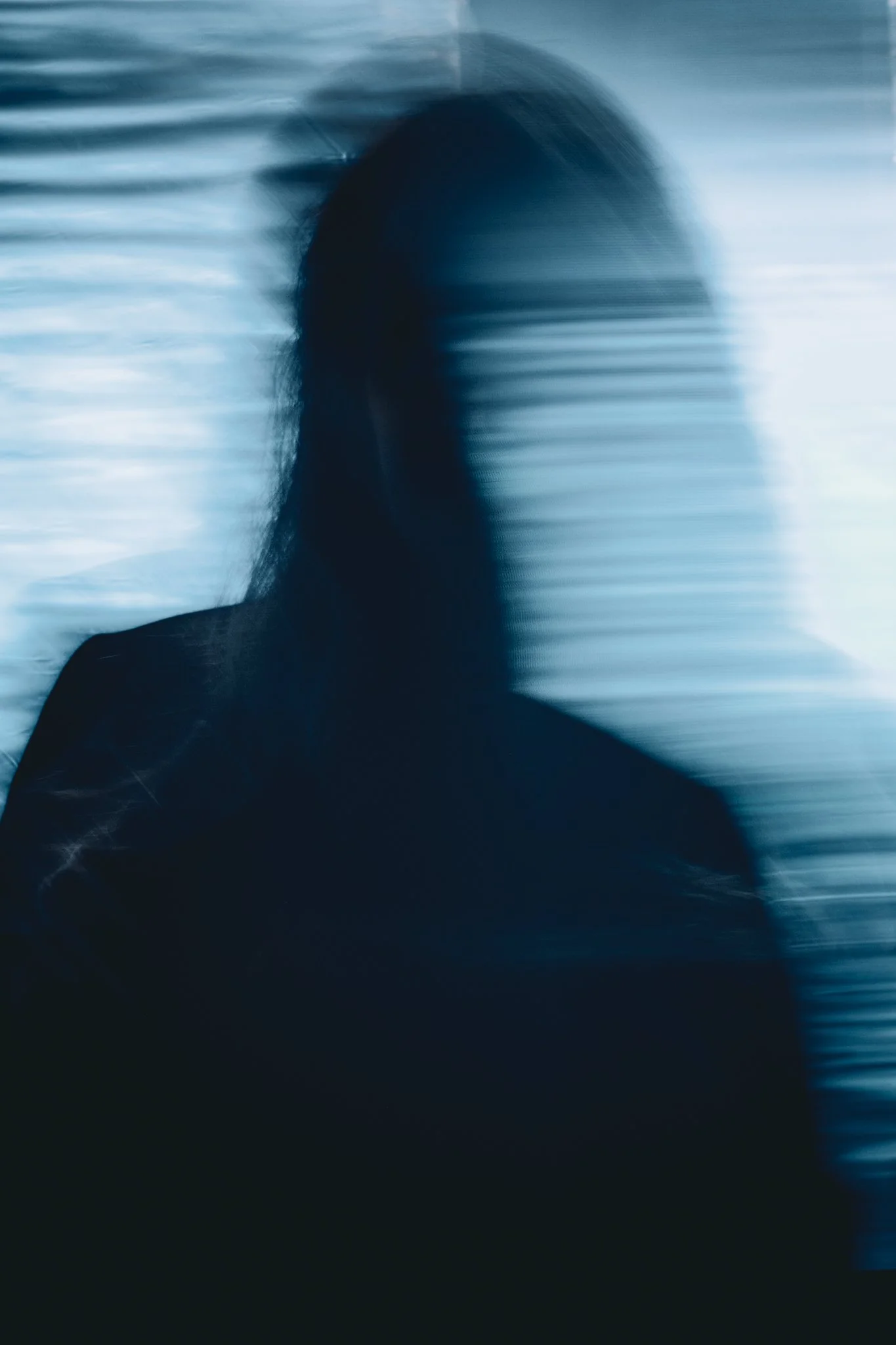Blurred silhouette of a person with long hair against a dark blue background with horizontal light streaks.