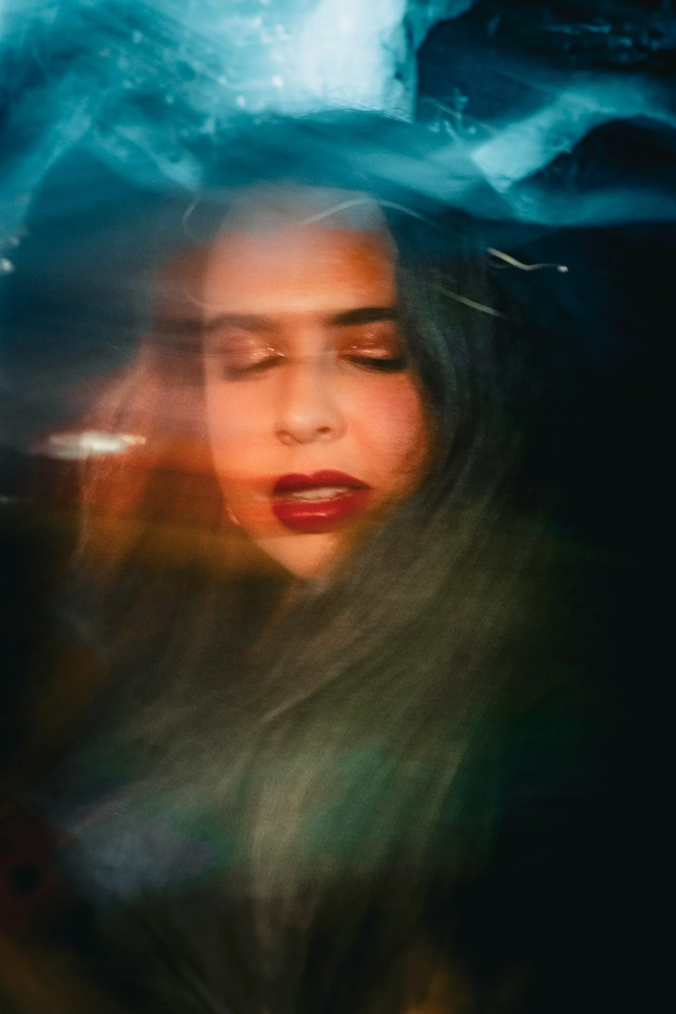 A woman with red lipstick and makeup with her eyes closed, surrounded by a swirling, abstract mixture of colors and textures.