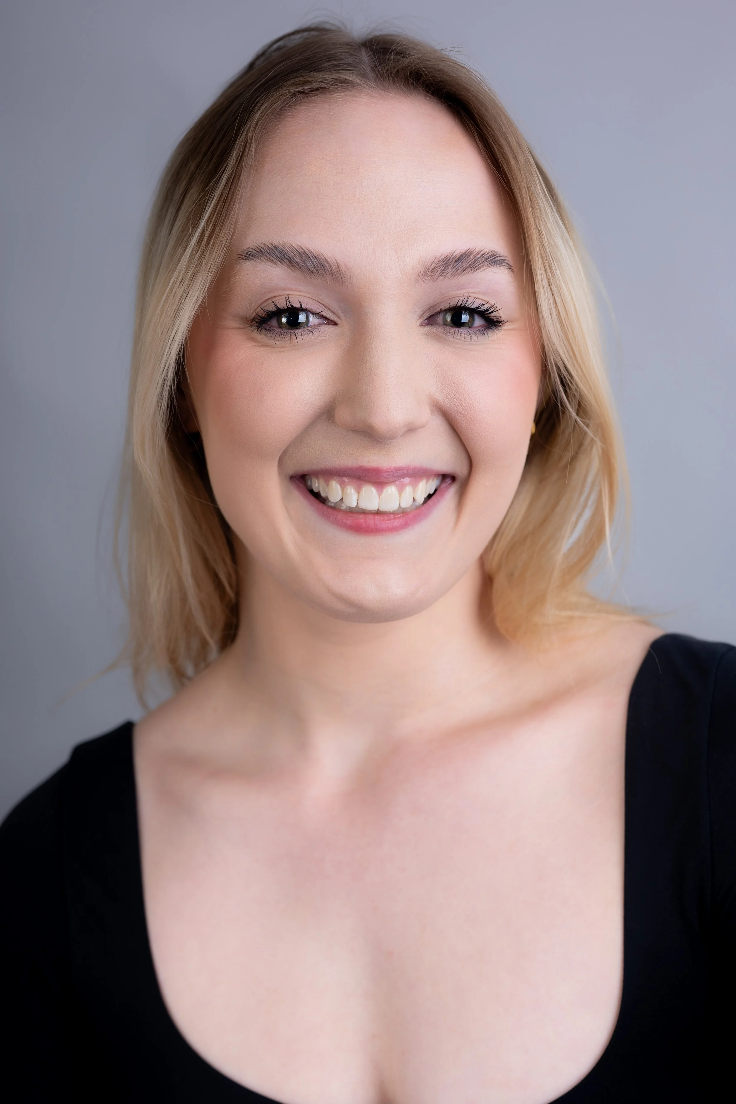 A woman with blonde hair smiling in a black top against a plain gray background.