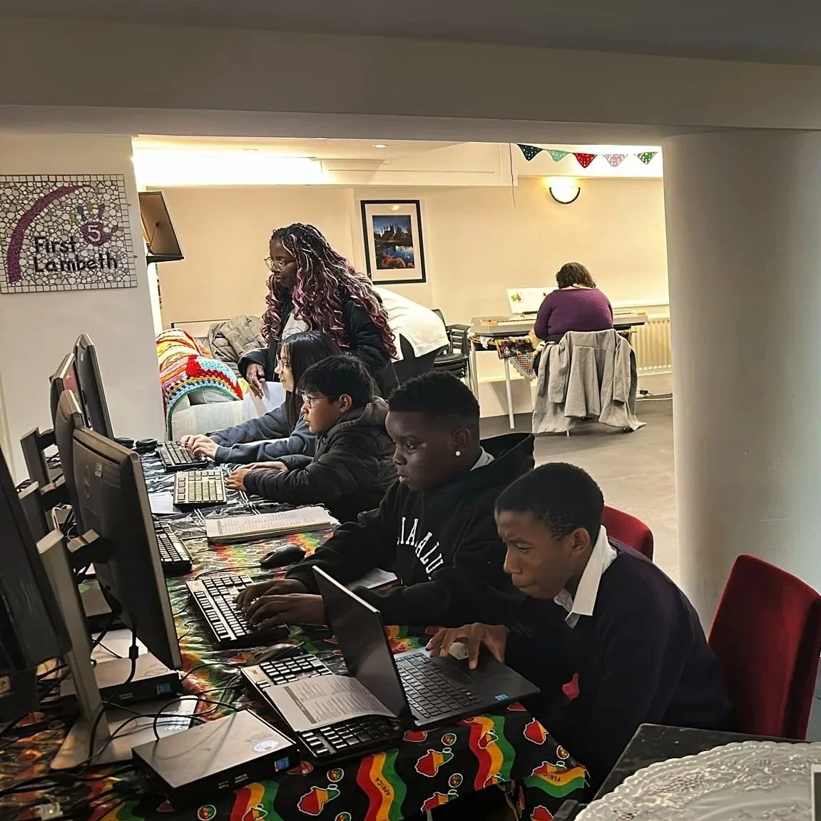 A group of young people working on computers at a computer station in a decorated room.