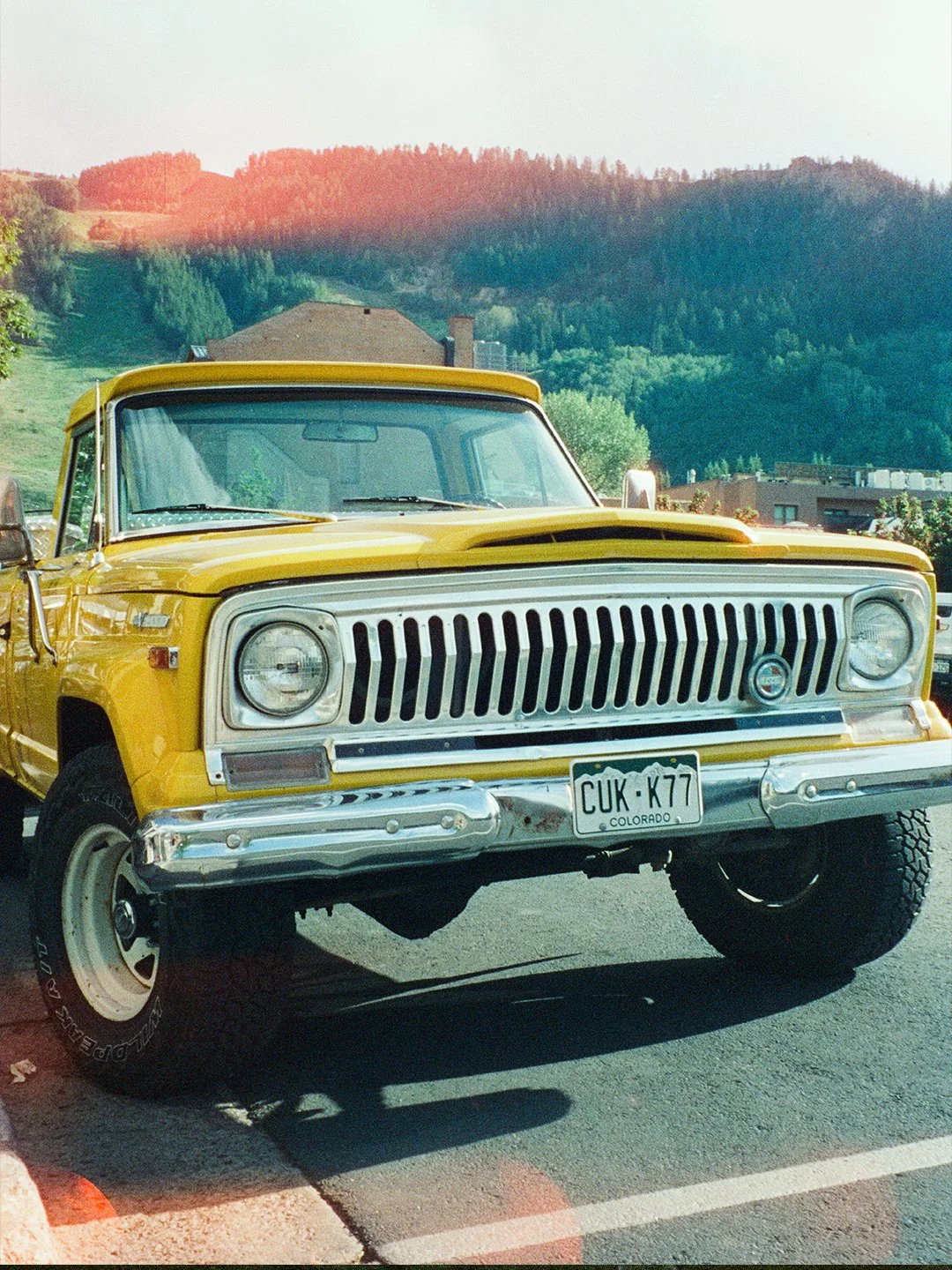 Yellow vintage off-road vehicle with Colorado license plate parked on street with mountain landscape in background.