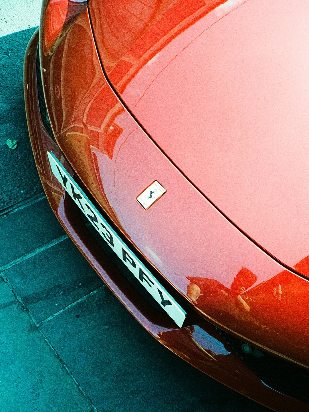 Red Ferrari sports car showing front end, license plate reading 'X23 BEY', and a Ferrari badge on the hood.