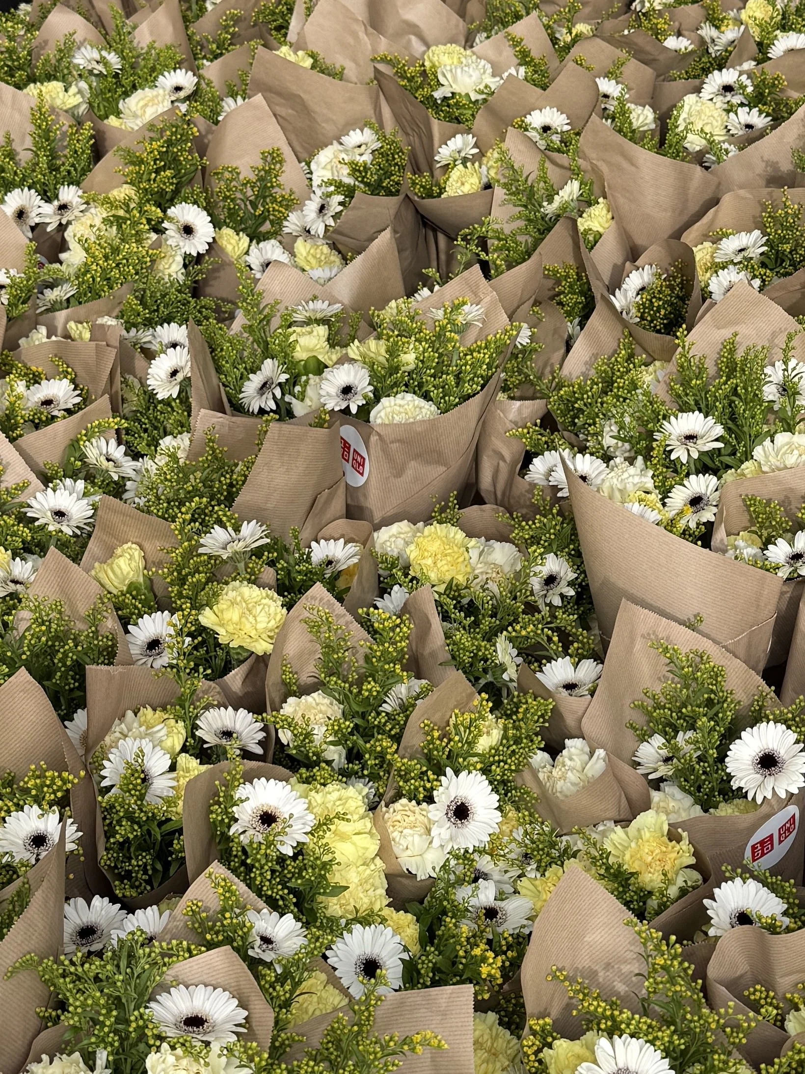 Multiple bouquets of yellow and white flowers wrapped in brown paper, arranged together.