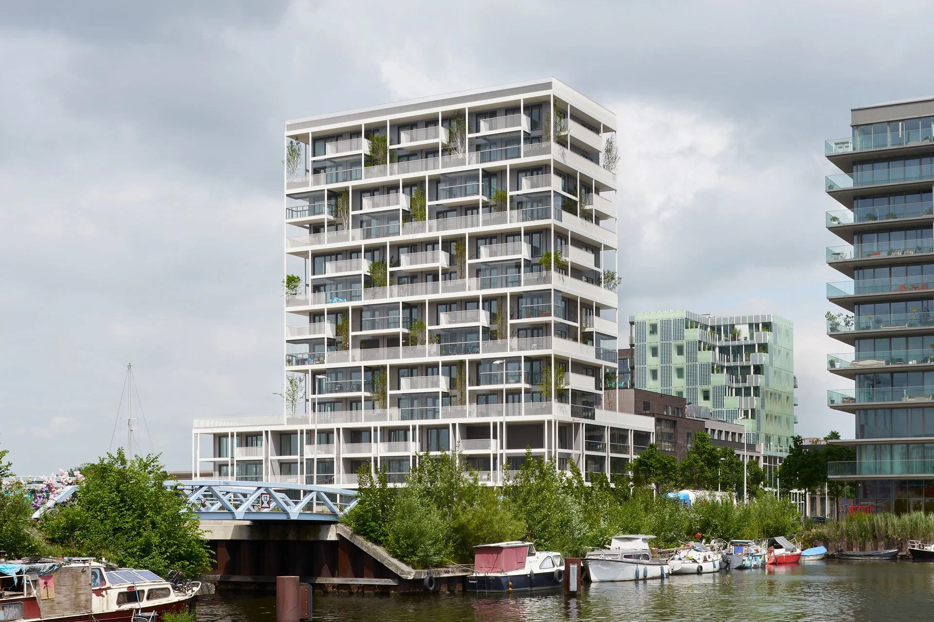 Modern multi-story residential building near a waterway with boats and greenery.