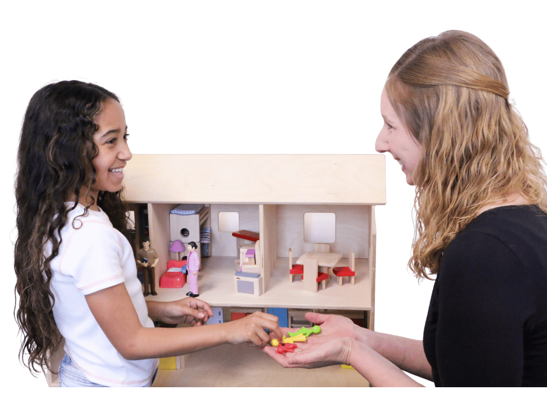 Girl smiling at therapist as she plays with dollhouse