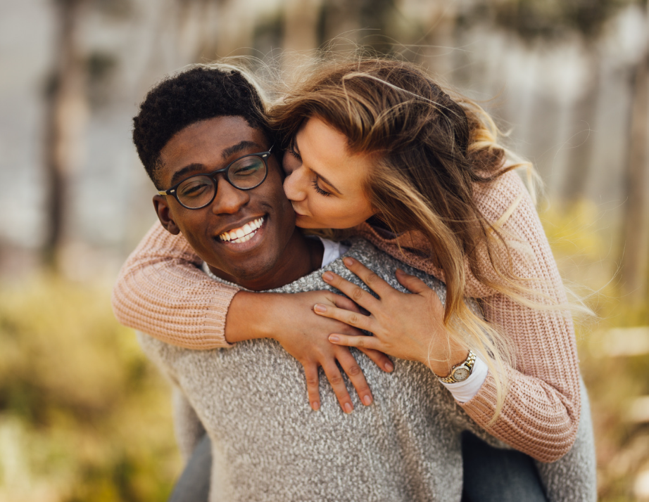 Woman hugging her smiling partner from behind and kissing his cheek, premarital counseling in Denton and Justin, TX