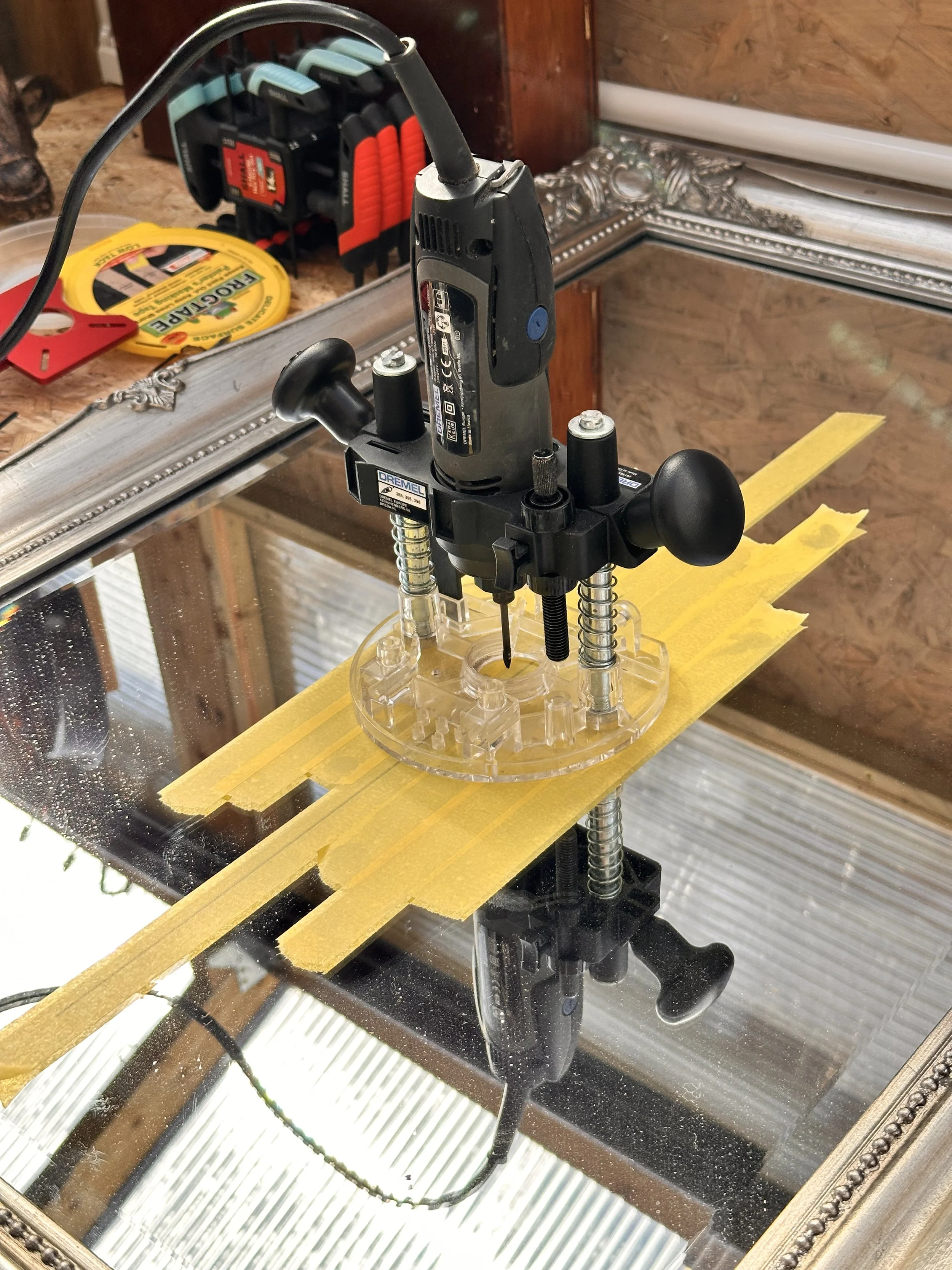 Dremel rotary tool fitted with a diamond-tip bit being used to drill a hole into the vintage mirror with yellow tape for precision – part of the wall mounting process for i identify as fabulous darling wall mirror art