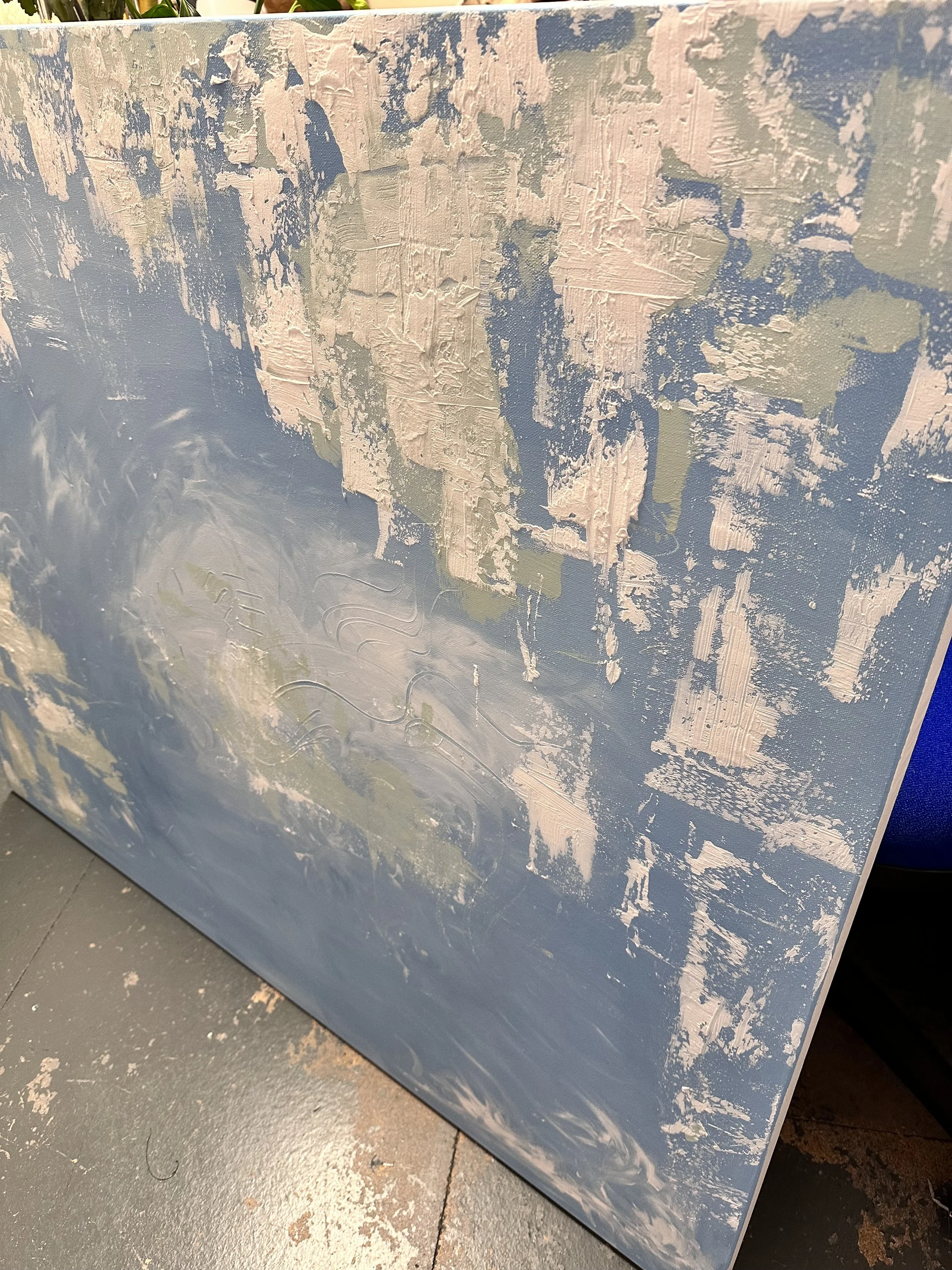 The early stage of the artwork weather or not showing rough, patchy textures in cool blue, white, and pale green tones across the canvas, on a grey floor.