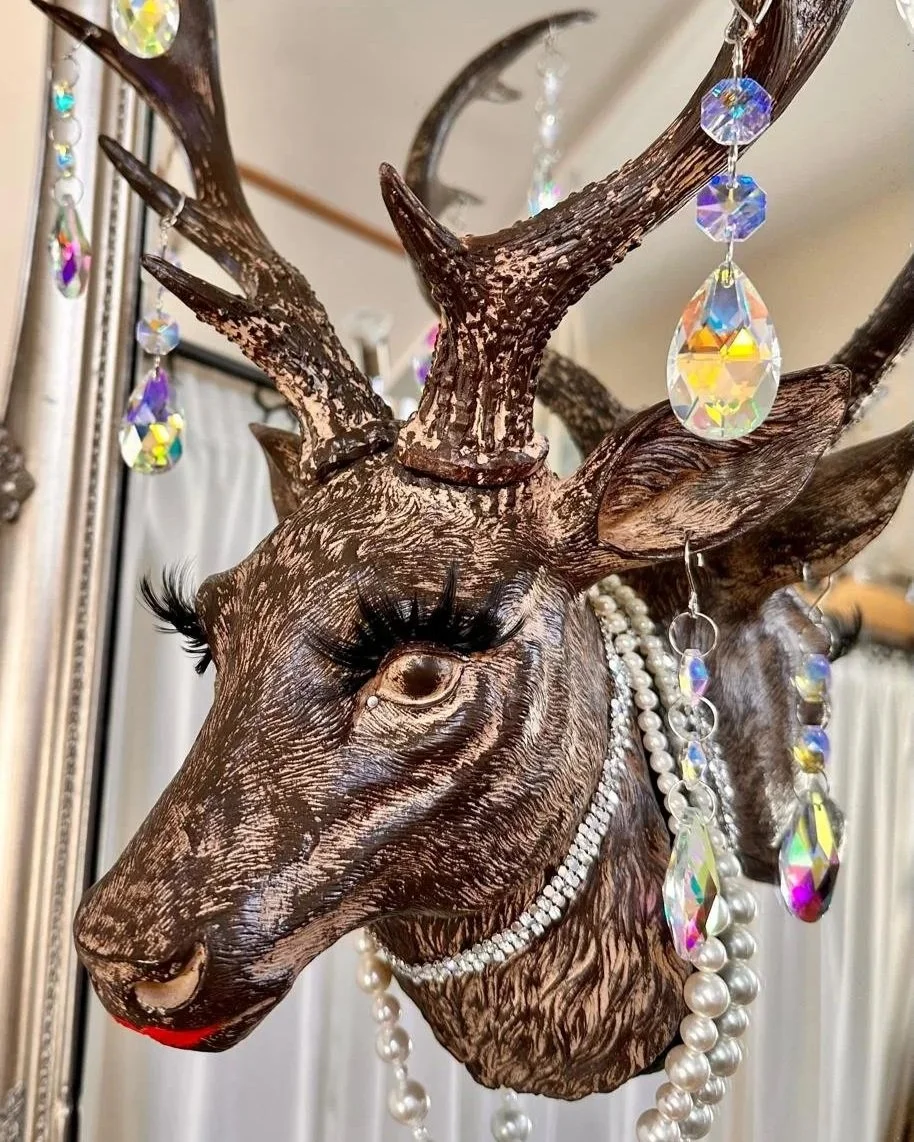 stags head inlaid into a mirror, the stag has bright red lipstick, large false eyelashes, a swarovski crystal chocker, crystal teardrop earrings and pearl necklace
