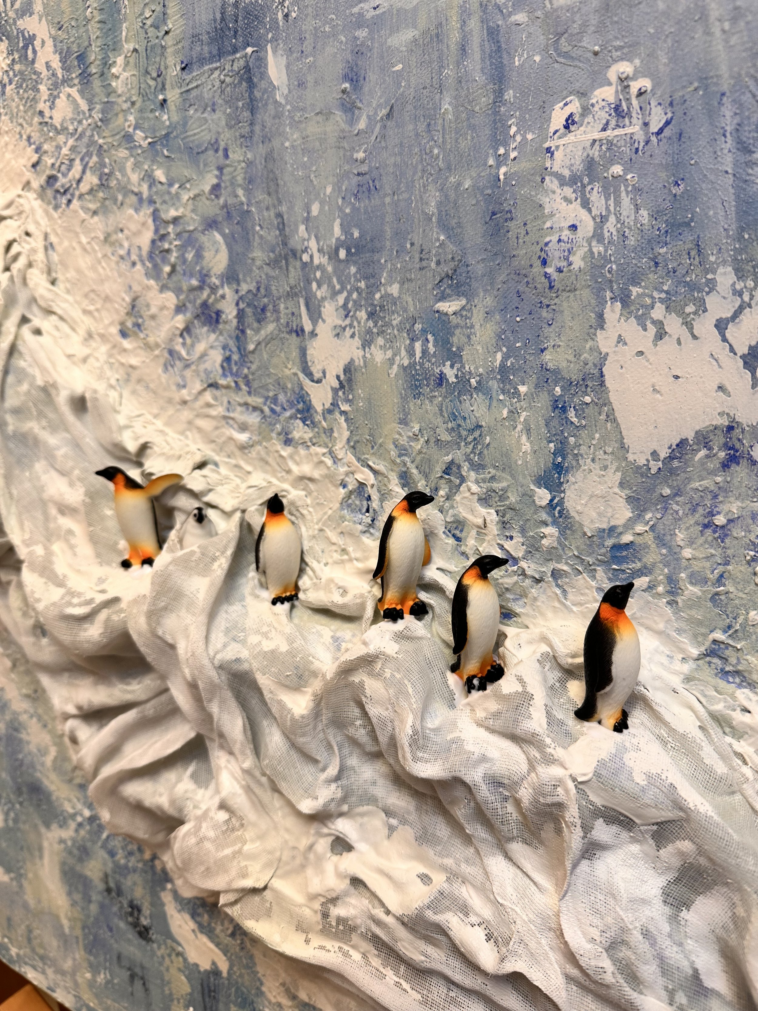 A detailed view of penguins and chicks nestled into the fabric folds, some climbing, some huddled. the blue, green and white painting part is clearly visible