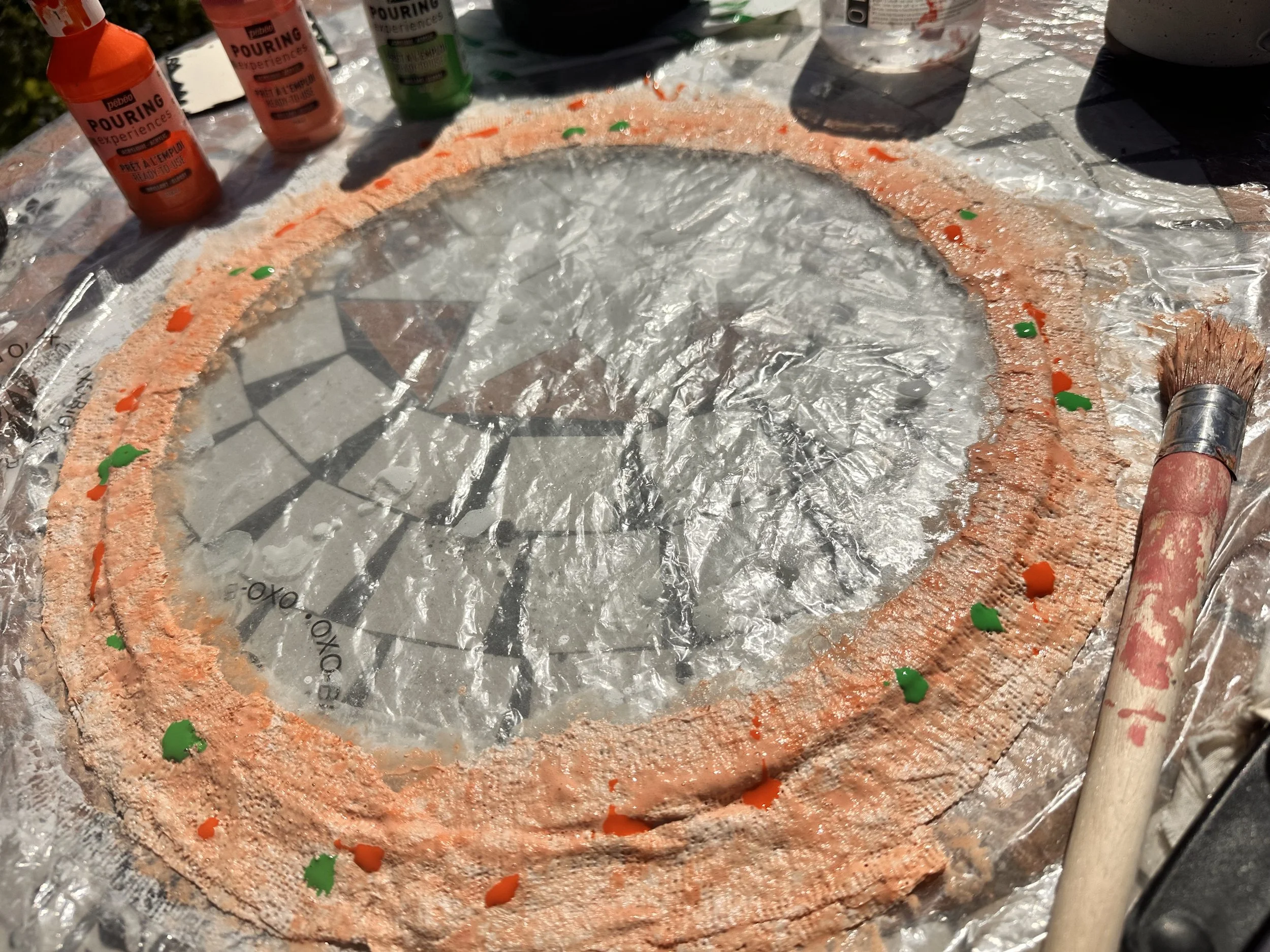 close up detail of the central brain section of the sculpture with the top having been cut off and pink toughened safety glass on a mosaic table being painted with pebeo green and orange fluid paints