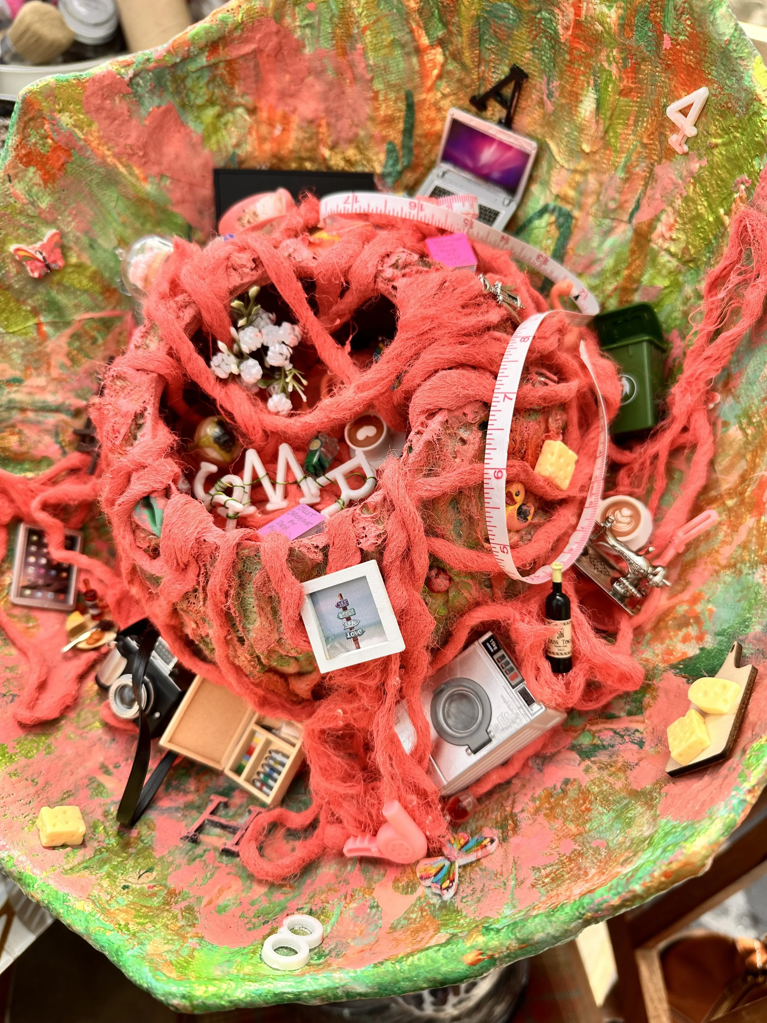 close up detail of the brain section of the meno brain sculpture with the top having been cut off and pink painted wool spilling over the edges and being refilled with found mini objects