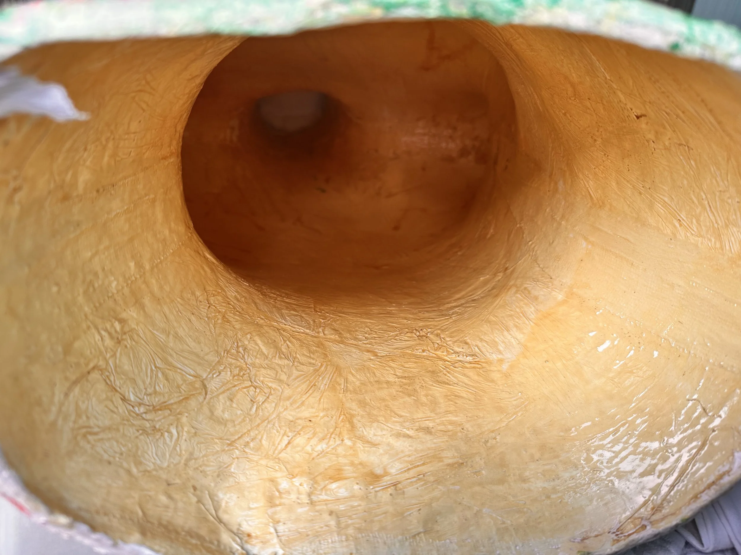 the meno brain sculpture’s hollow interior. The inside of the torso is coated in glossy resin, glowing with rich amber-gold tones. It looks warm and womb-like a safe glowing space that contrasts with the clutter above.