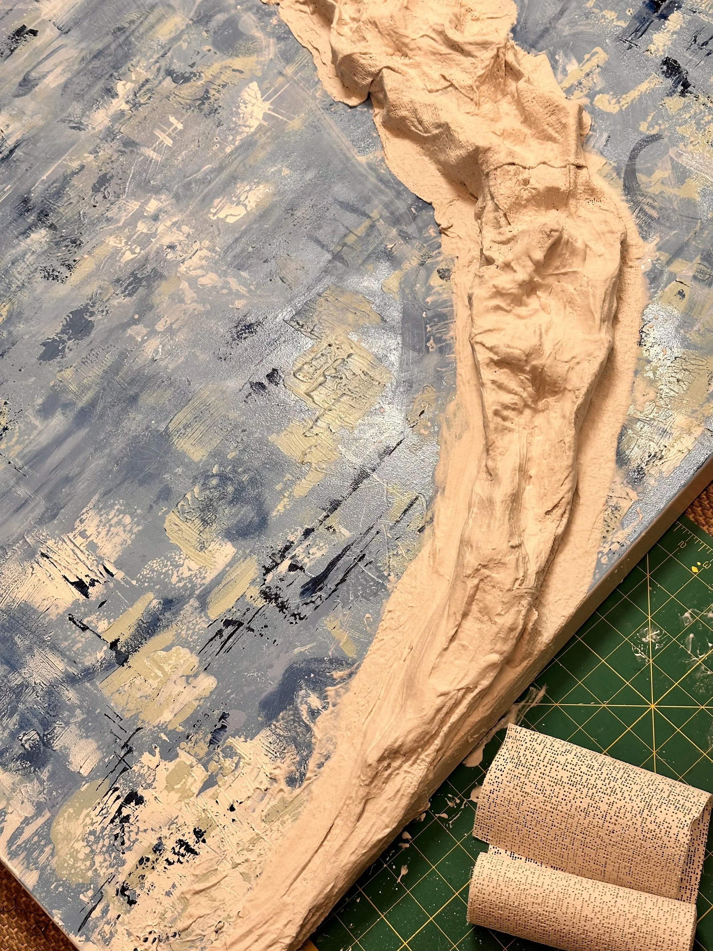 A strip of modroc fabric is beginning to be sculpted diagonally across the painting, suggesting a slope or ledge on the blue, green and white painted mixed media canvas painting