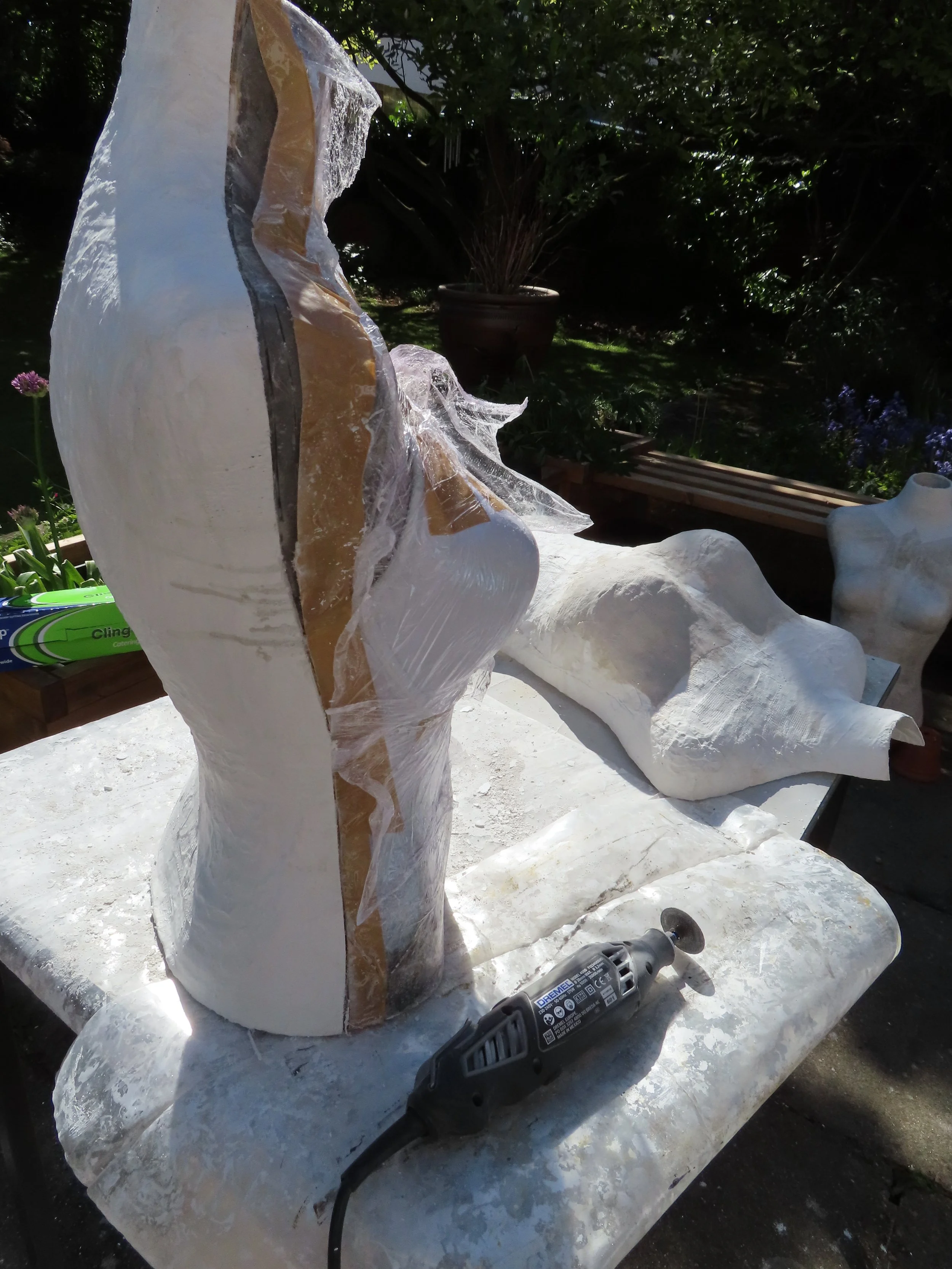 A side shot showing the sculpted torso being sliced down the side using a Dremel tool,  front of the cast is laying on a table trying. A second bust is seen drying on the ground
