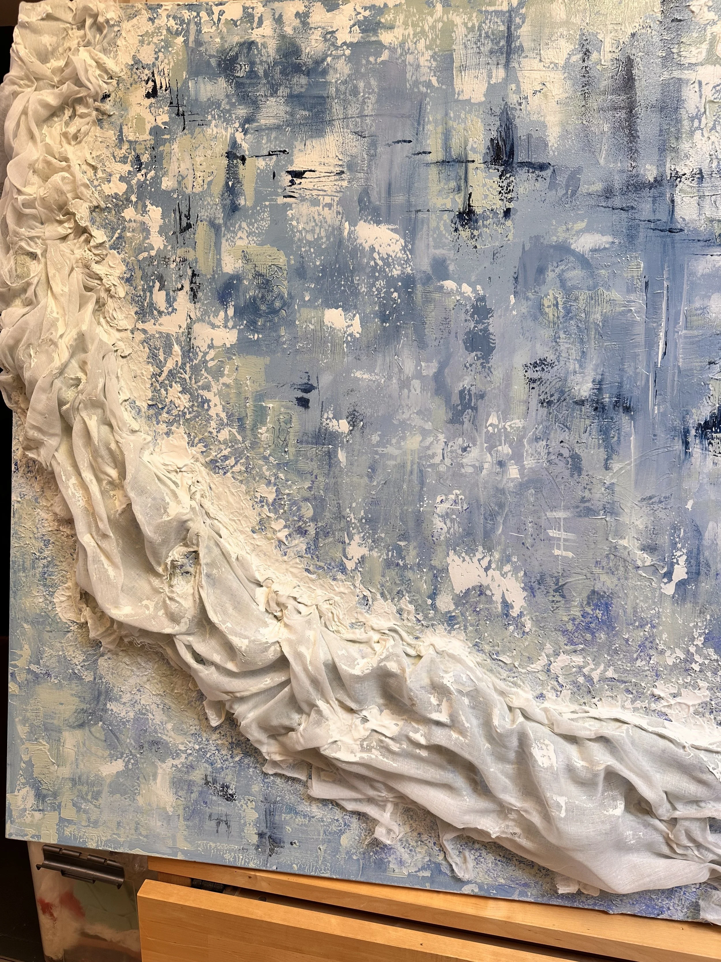 Close-up of the snow-textured cotton and muslin ledge integrated into the blue green and white painted canvas, the canvas sits on a wooden table